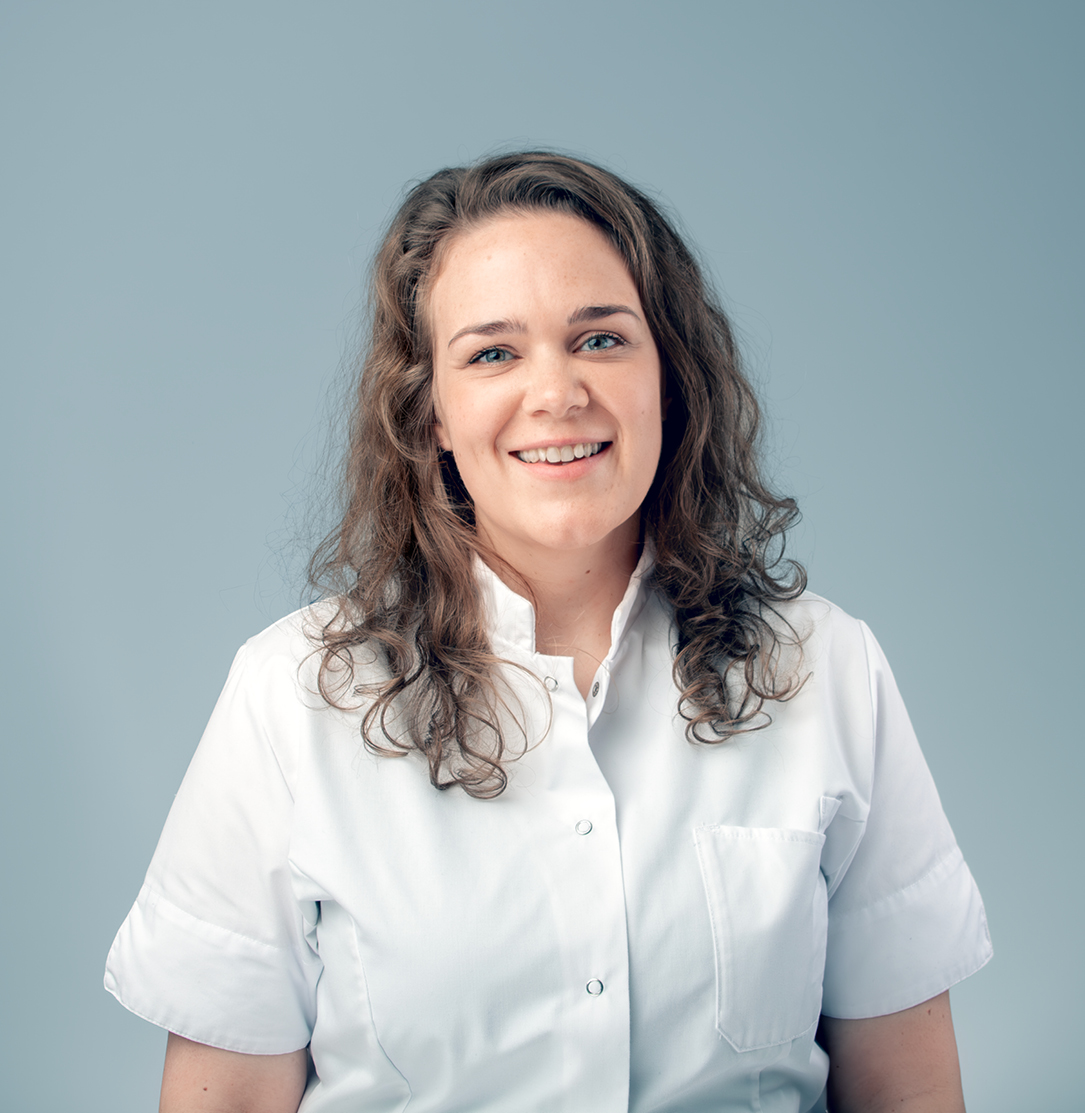 Portret Jane Overmars, glimlachend op lichtblauwe achtergrond. 