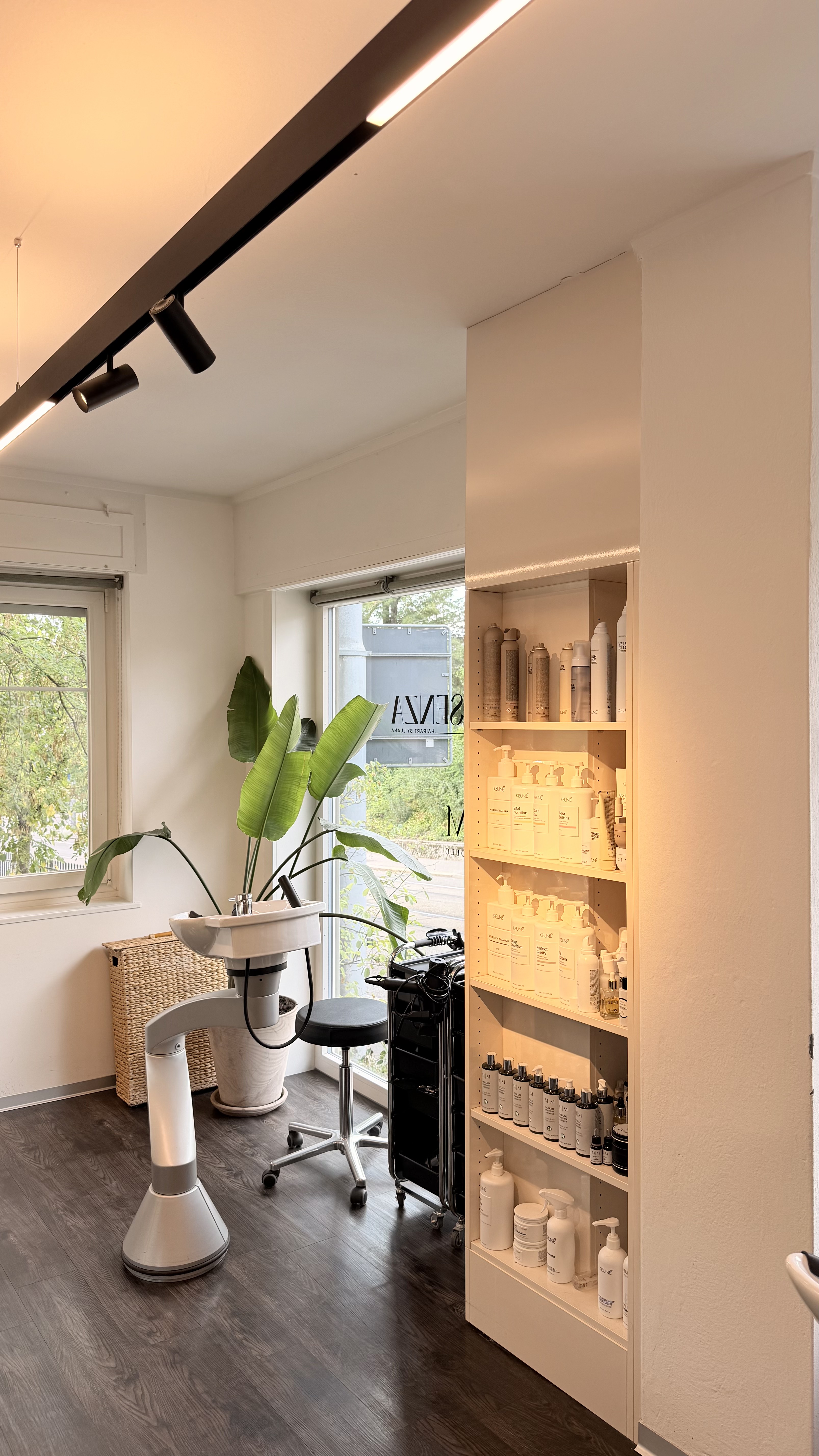 Warm beleuchtetes Produktregal und Waschplatz im Coiffeur L’assenza Zürich
