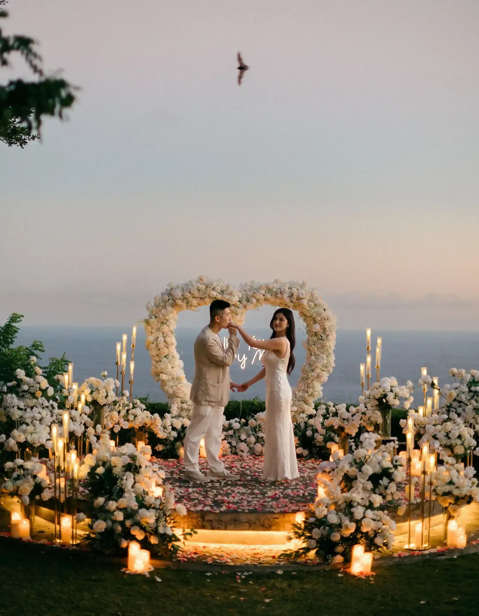 Cliffside engagement proposal setup in Bali with heart-shaped flower arch at sunset
