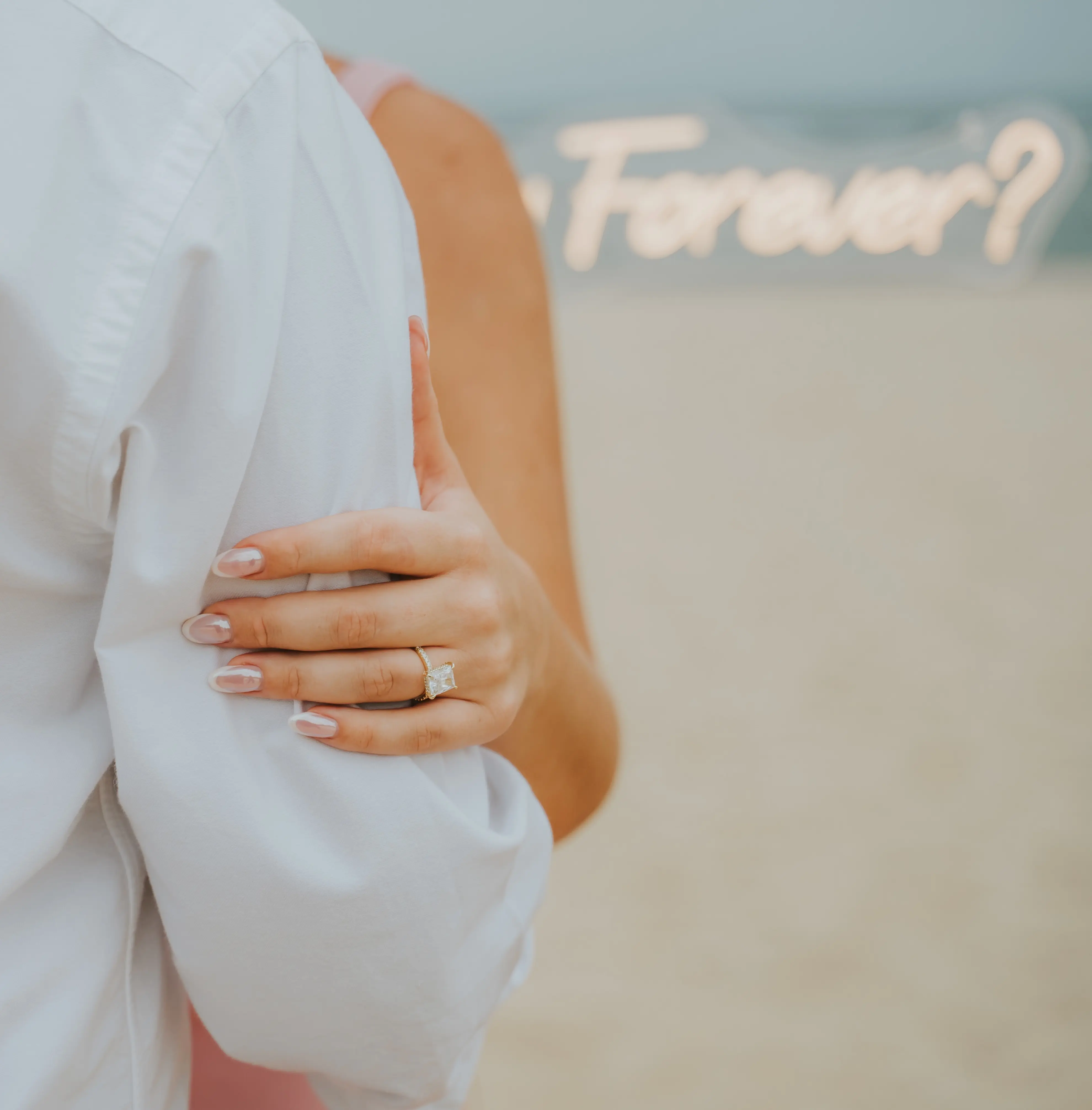 Woman showing engagement ring with 'Will you be my Forever?' neon sign