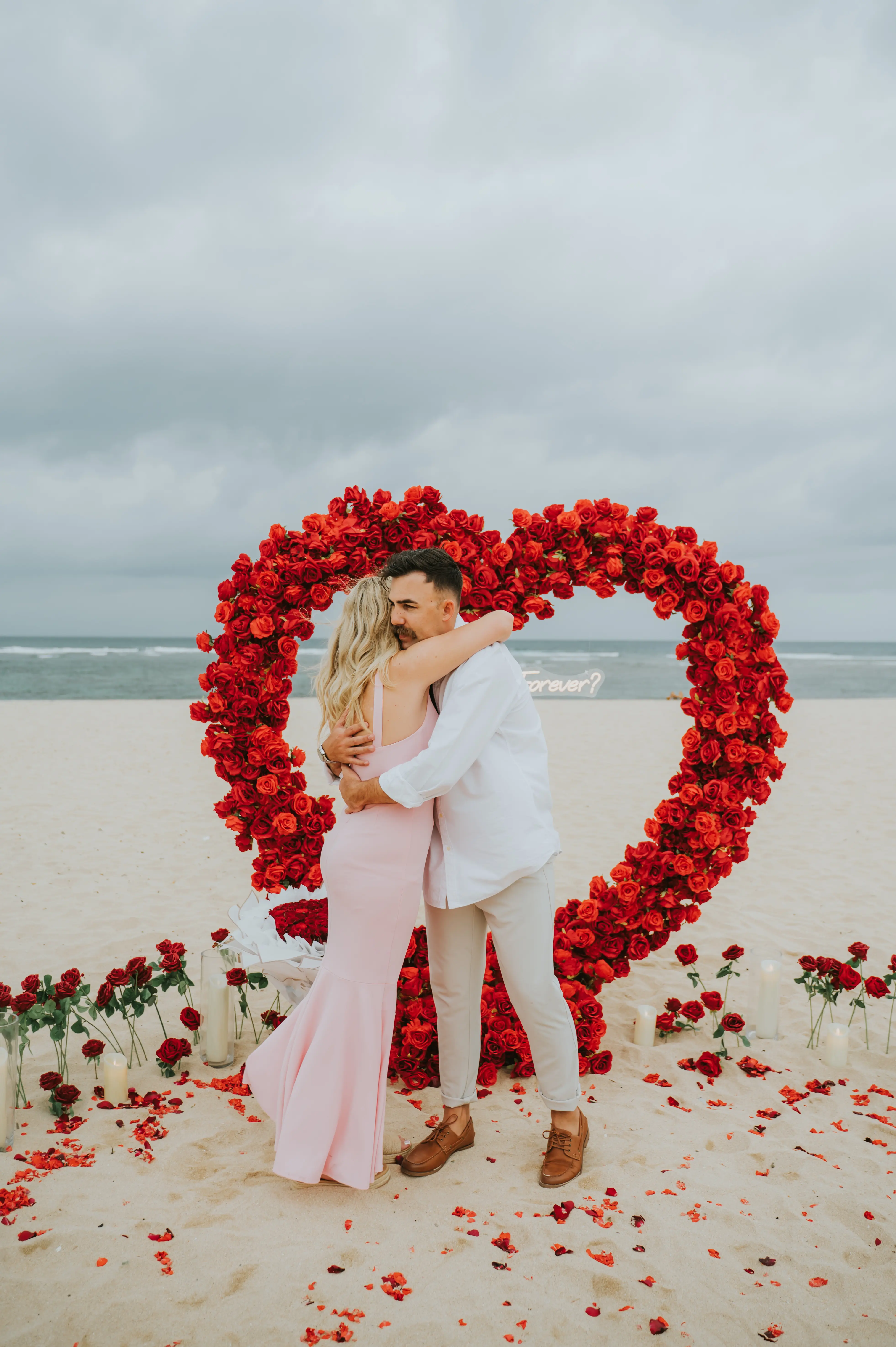 Proposal in Bali with couple hugging in front of red flower heart arch