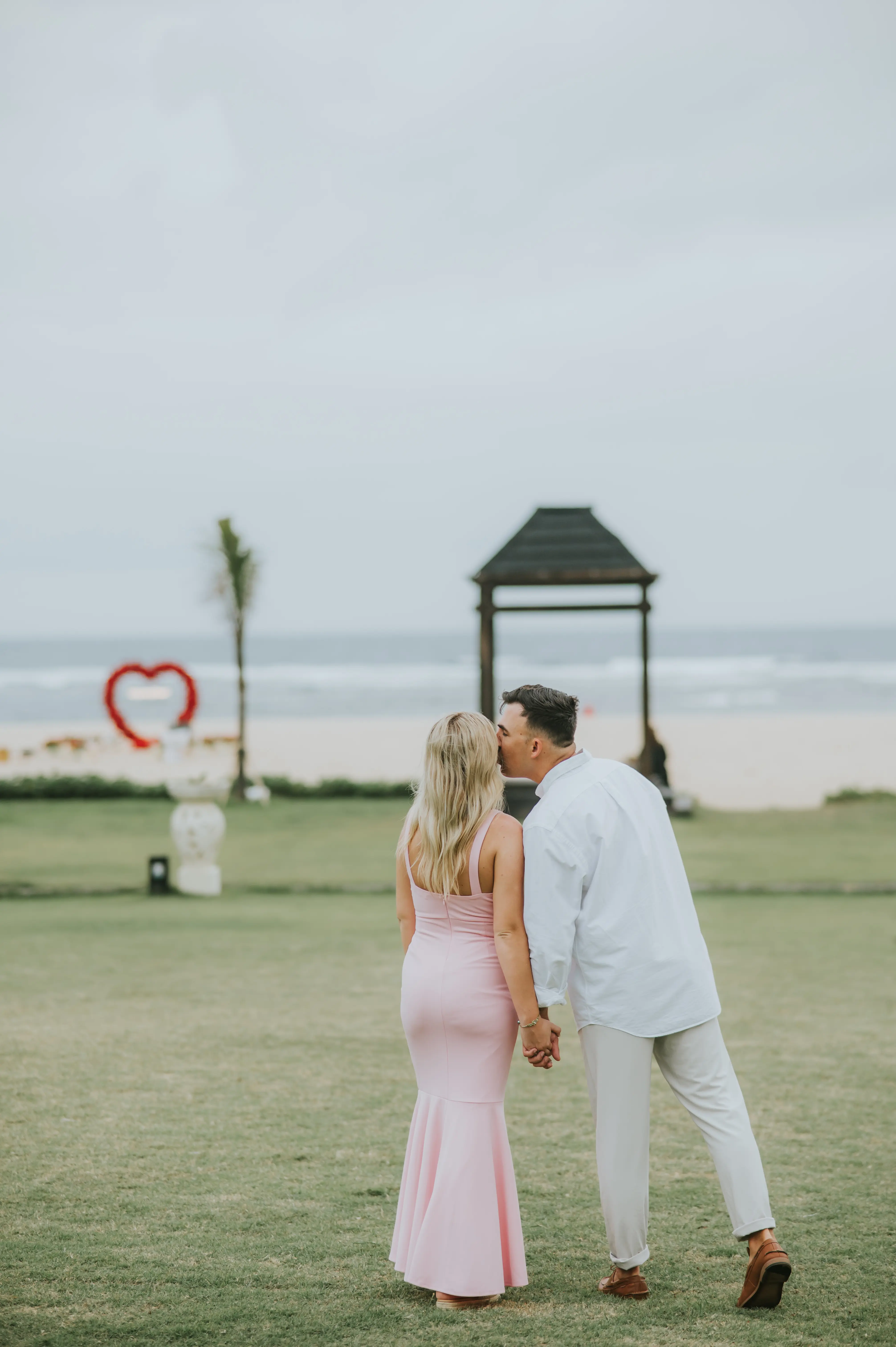 Couple walking under beach pavilion with heart-shaped rose arch in Bali
