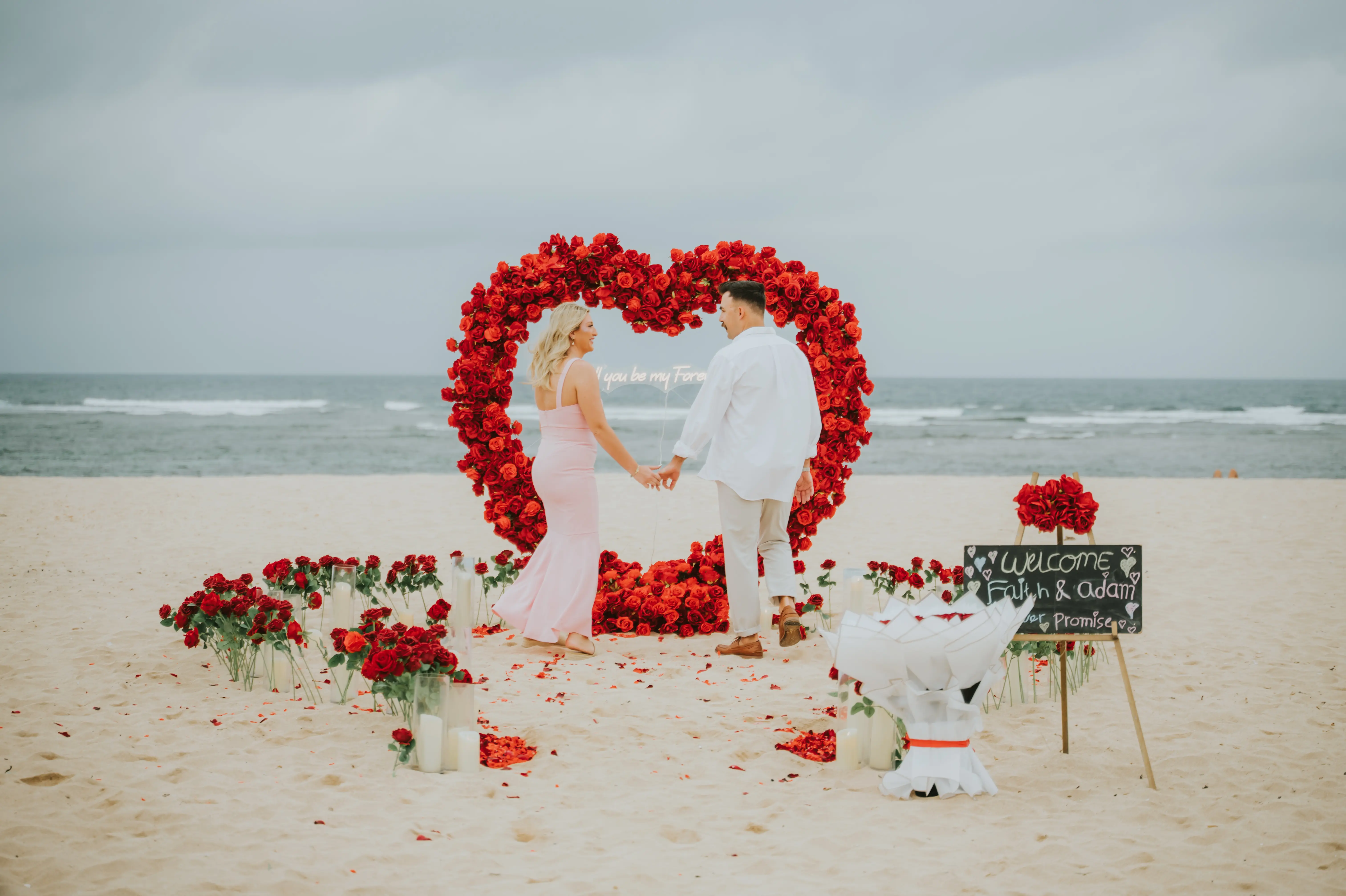 Romantic beach proposal setup with red rose heart arch in Bali at sunset