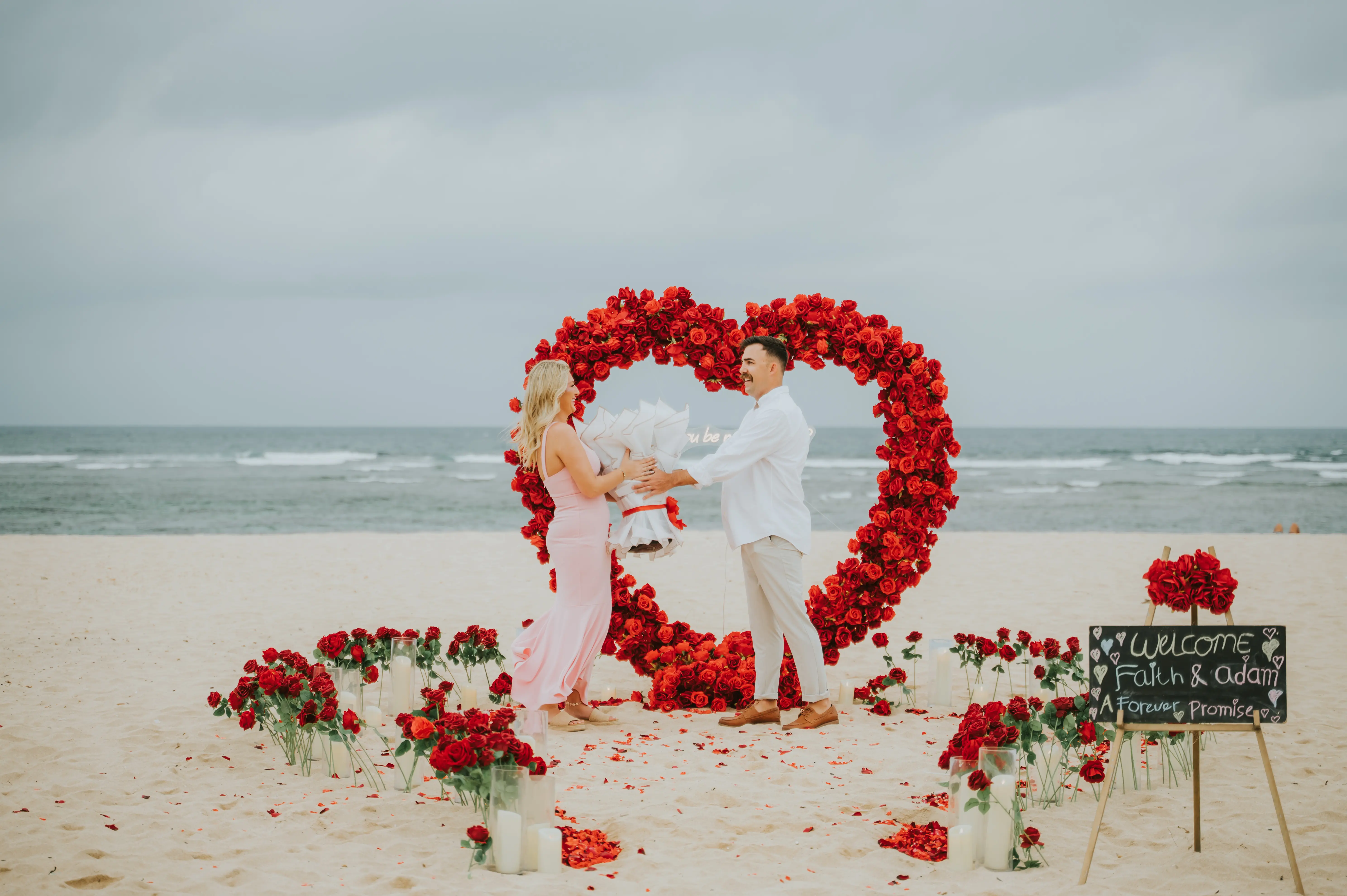 Heart-shaped red rose arch on the beach during cloudy Bali engagement