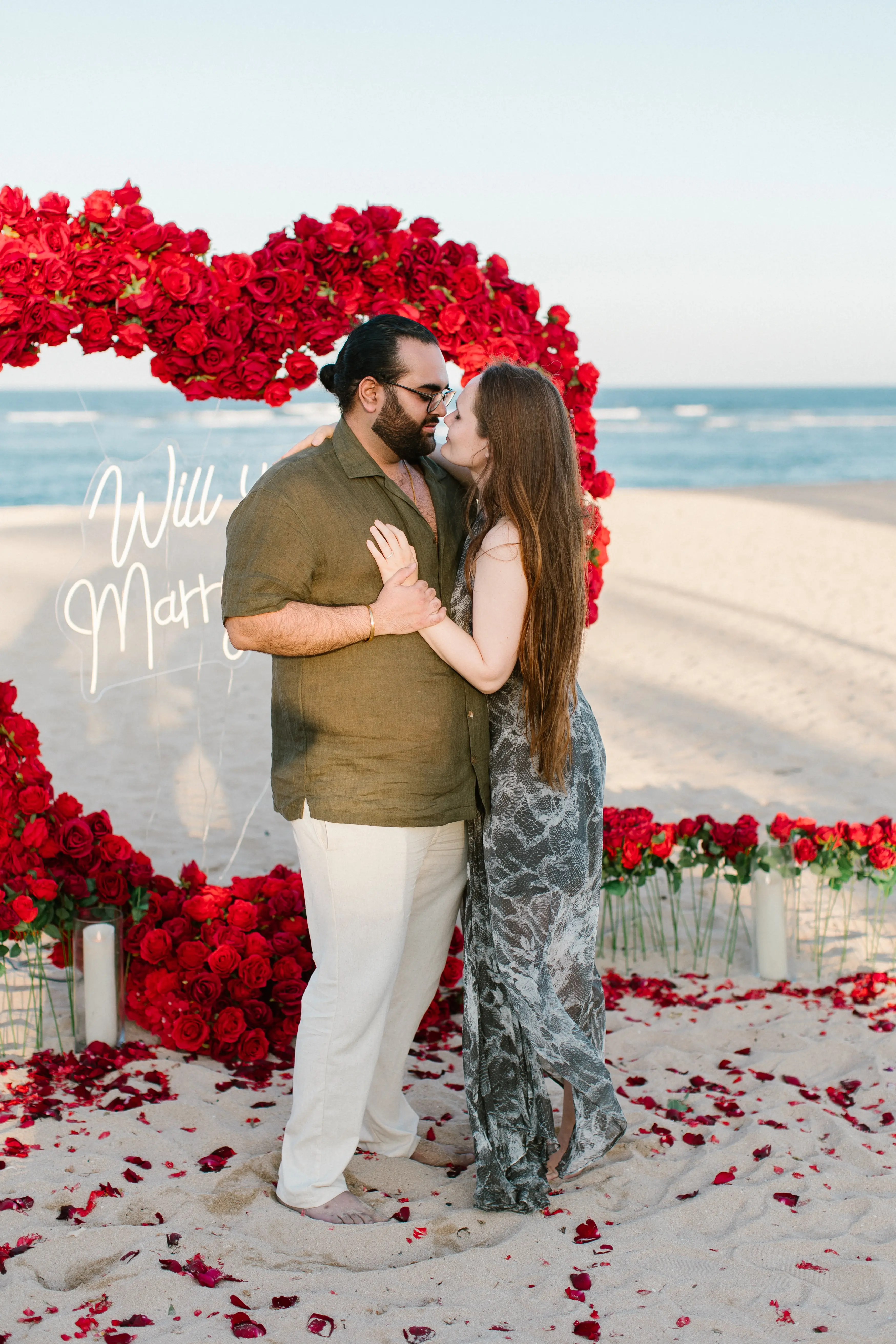 Couple kissing inside heart-shaped flower arrangement during Bali proposal