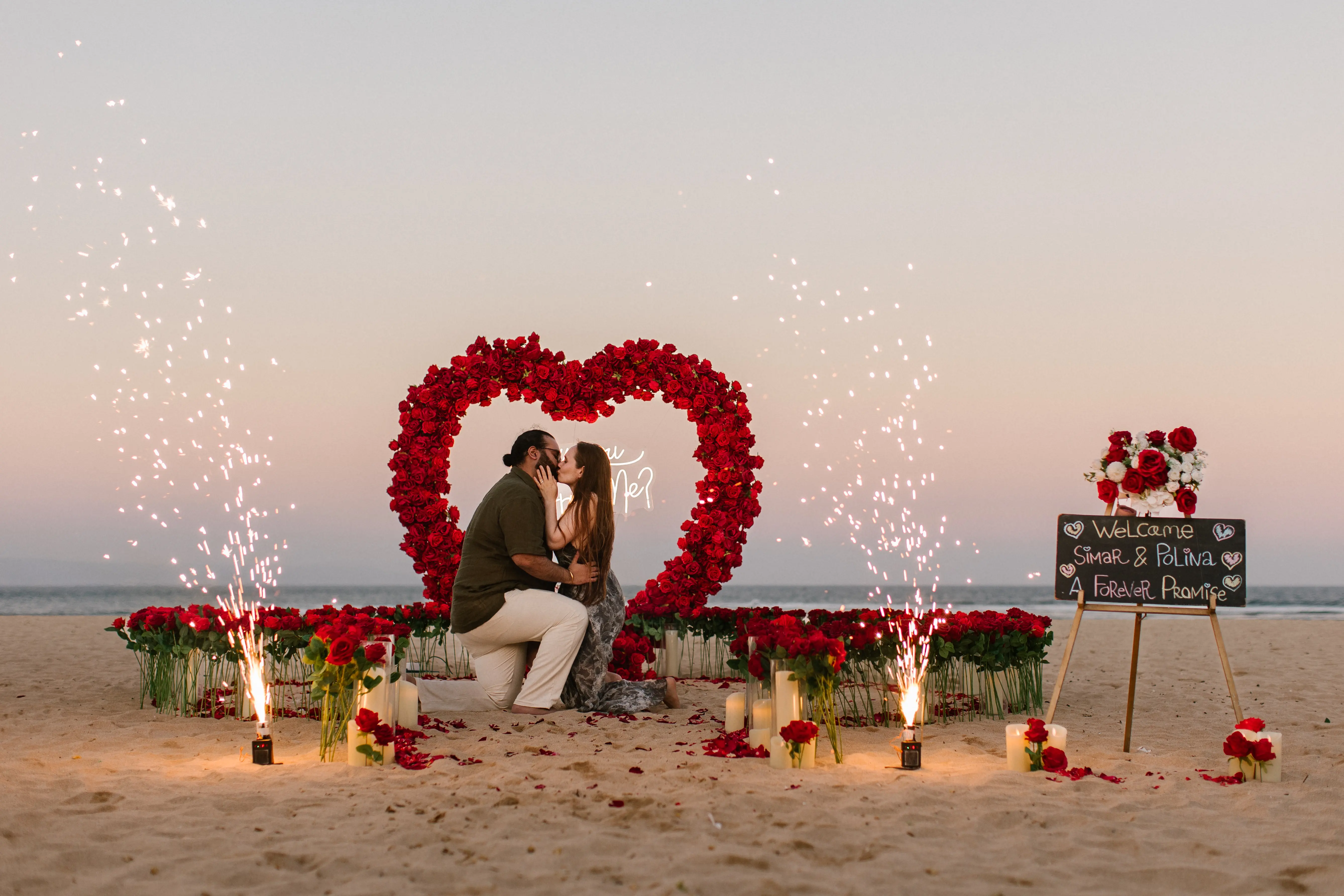 Romantic beach marriage proposal setup in Bali with heart-shaped flowers and candles at sunset