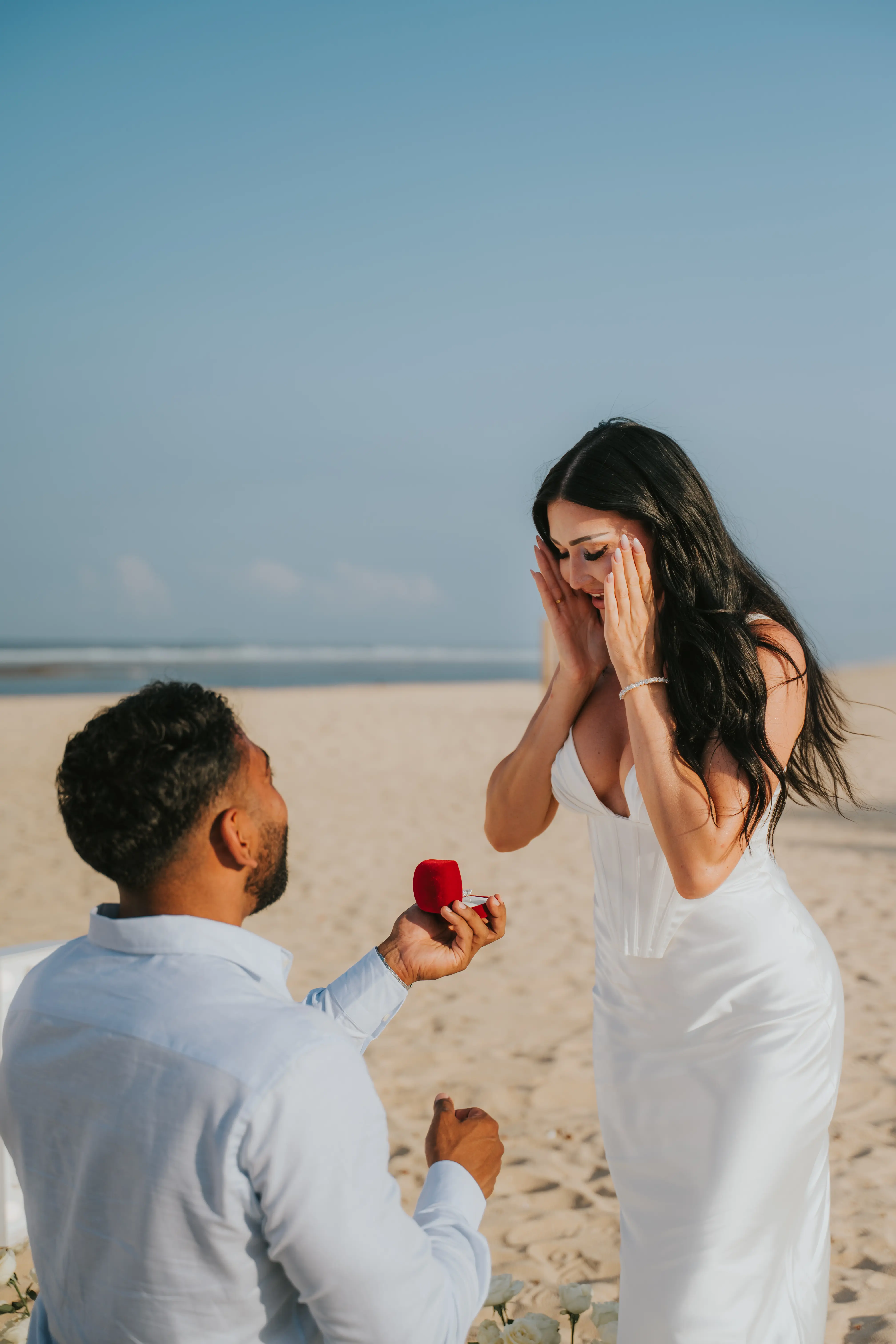 Groom on one knee proposing at sunset on Bali beach.