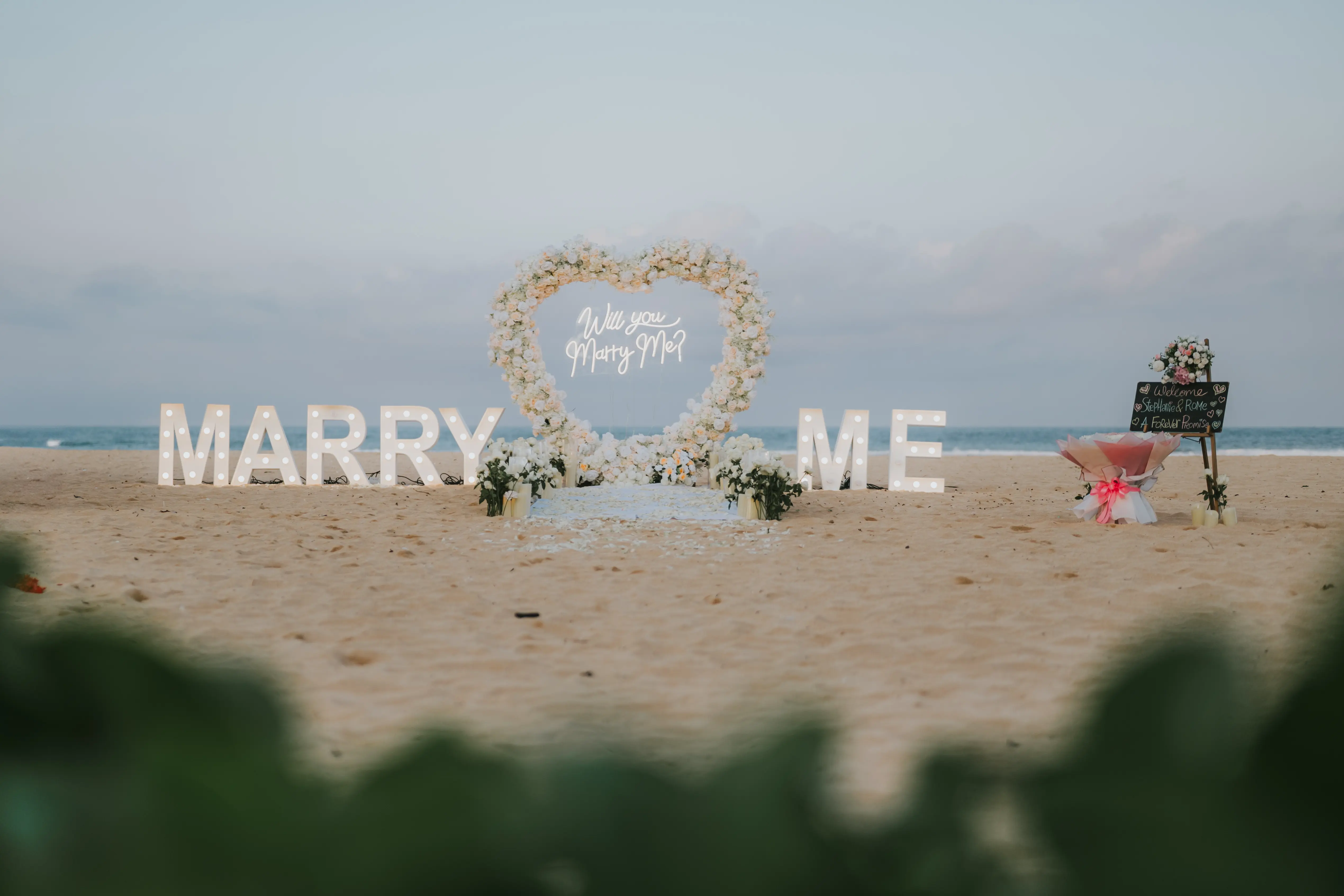 White-themed proposal setup with candles and floral arch on Bali beach.