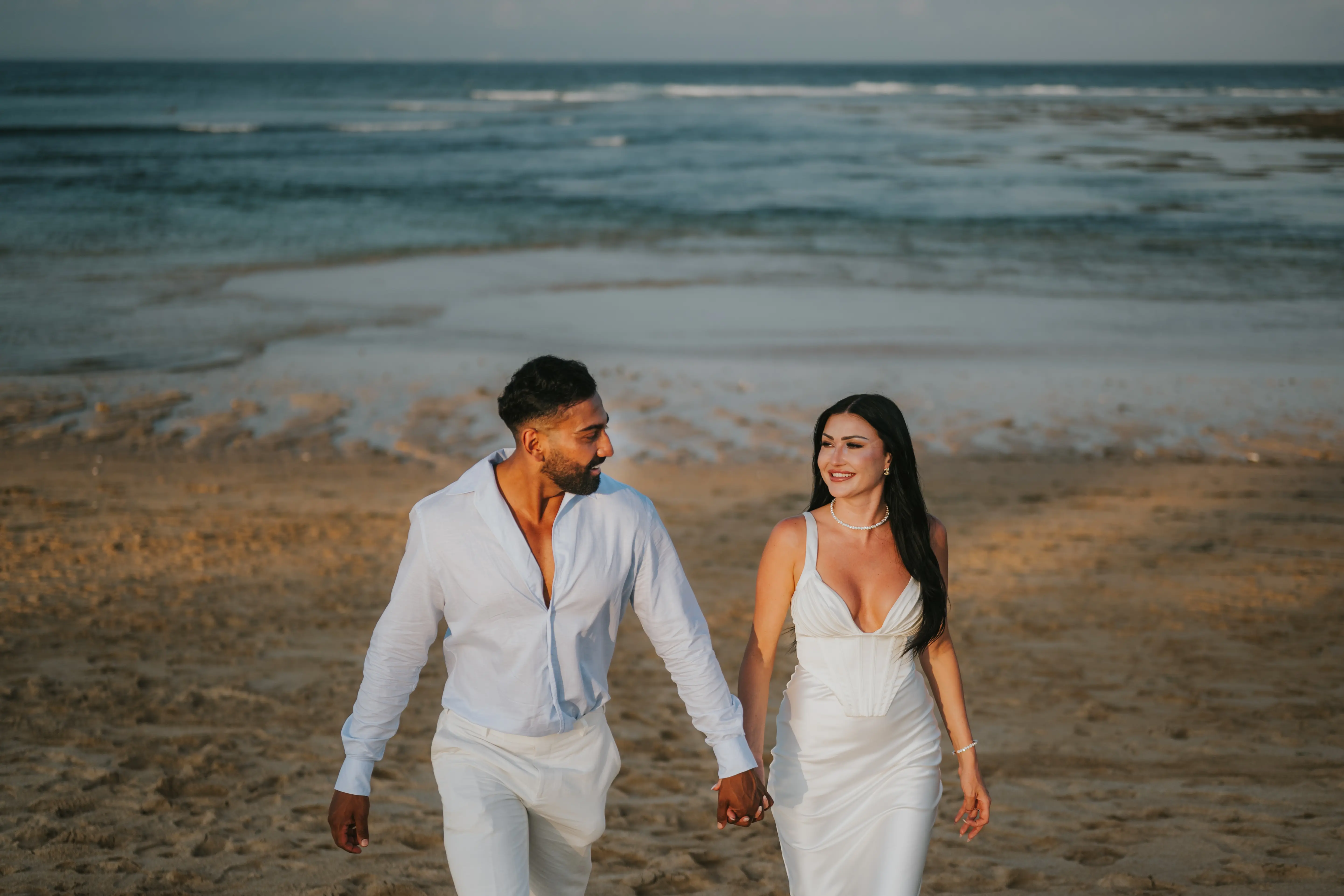 Couple walking hand in hand on Bali beach before proposal.