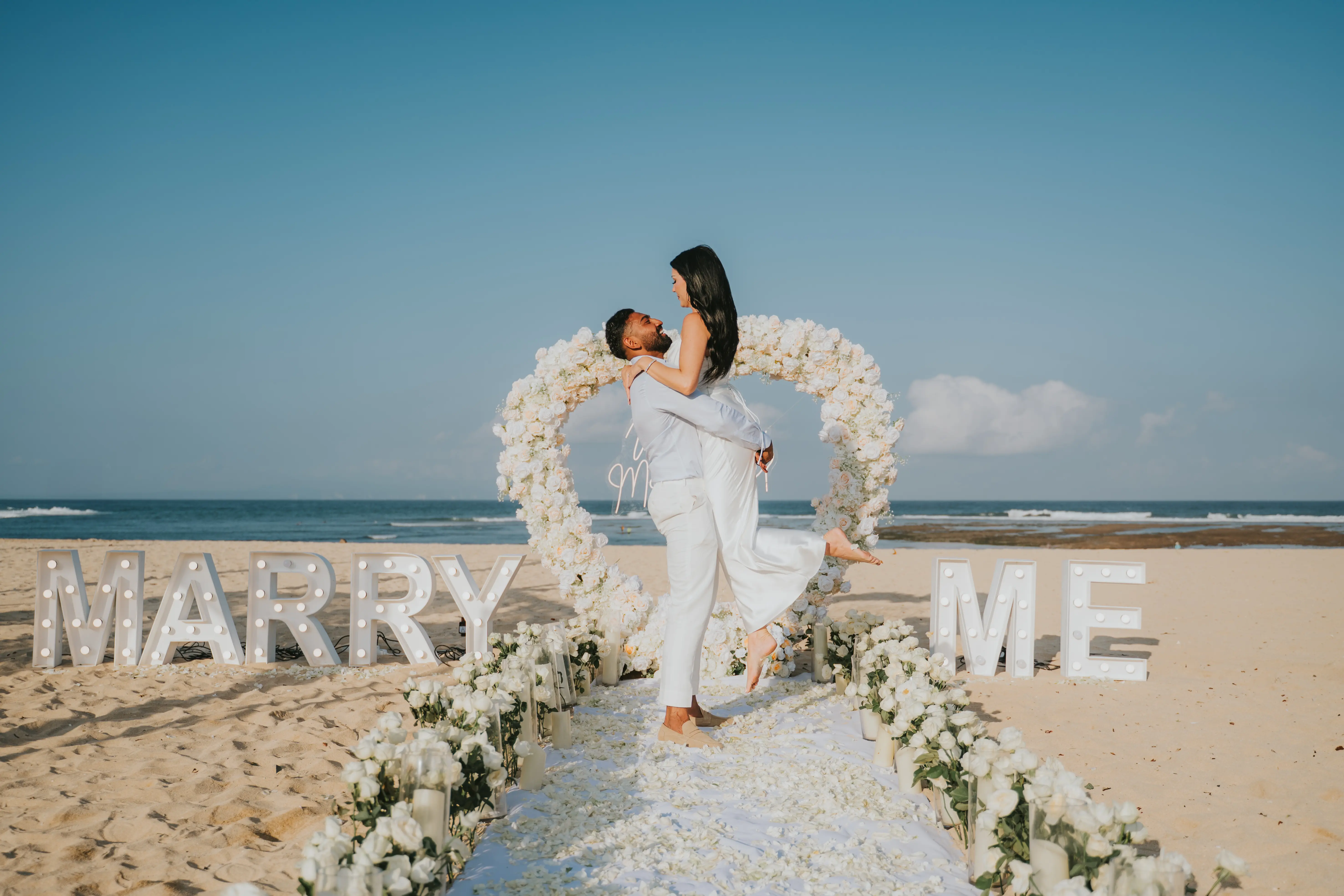 Bride in white dress standing inside floral heart arch.