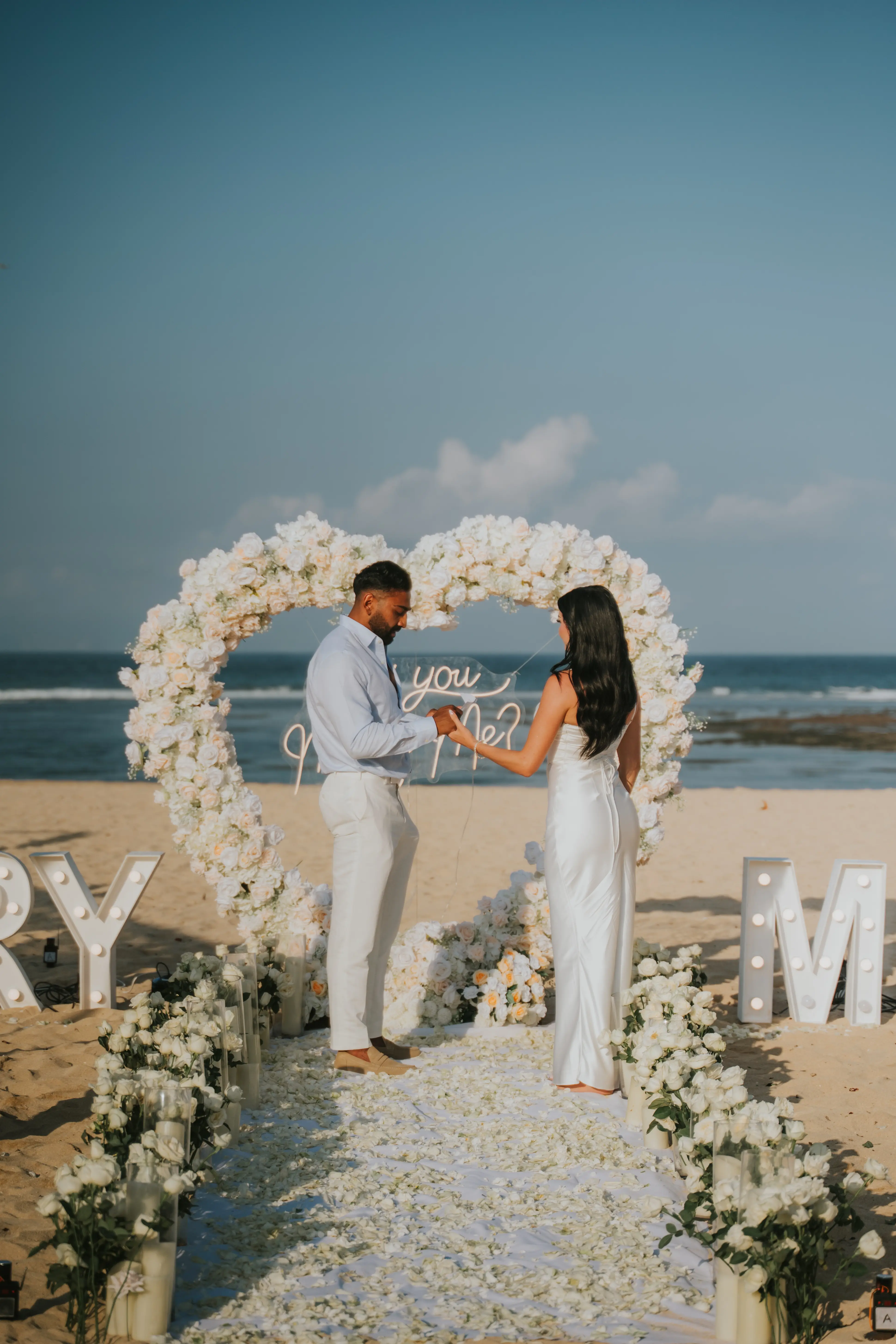 Bride posing with bouquet in front of floral arch at beach proposal.