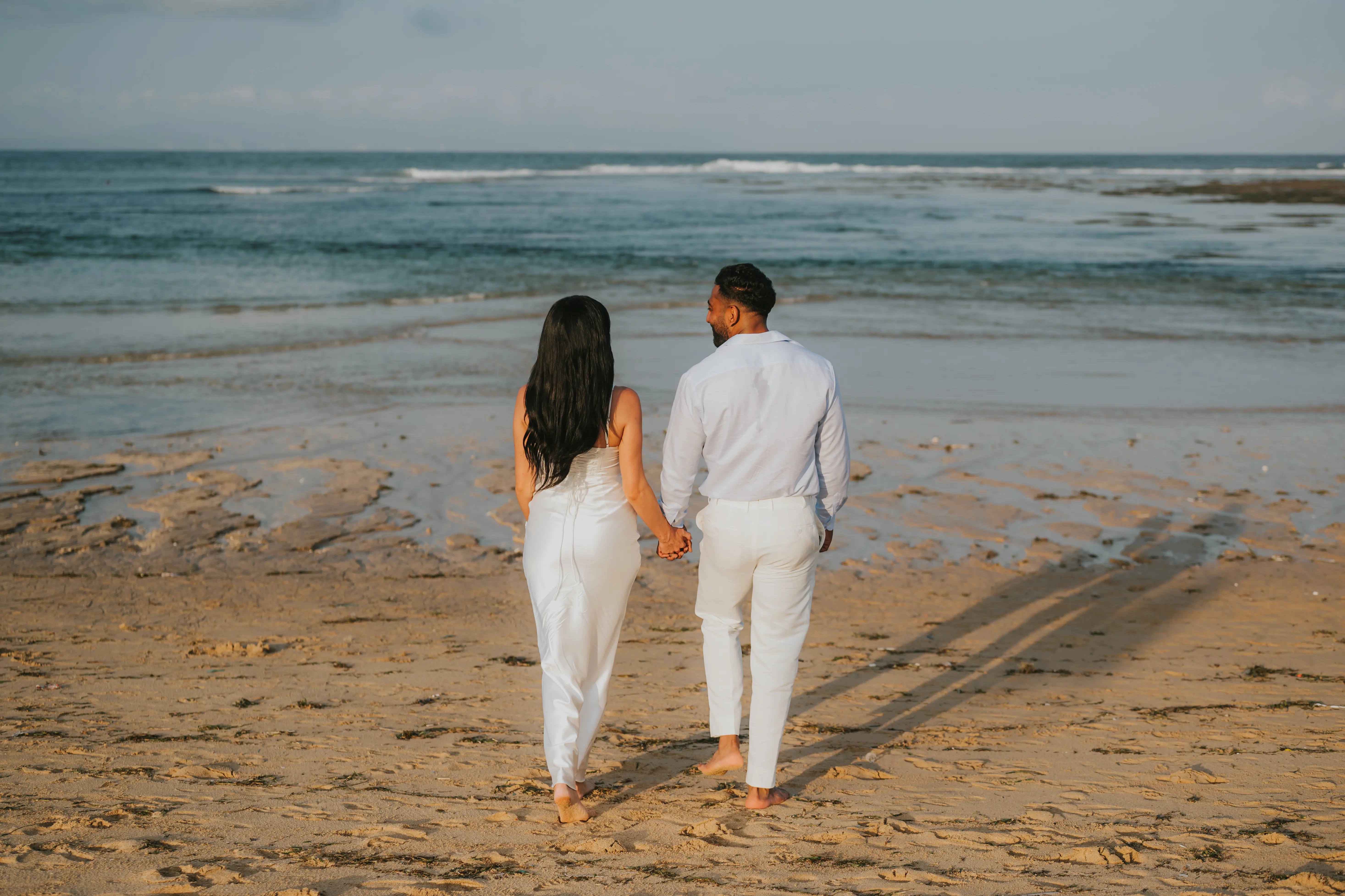 Couple walking barefoot along the shoreline after engagement.