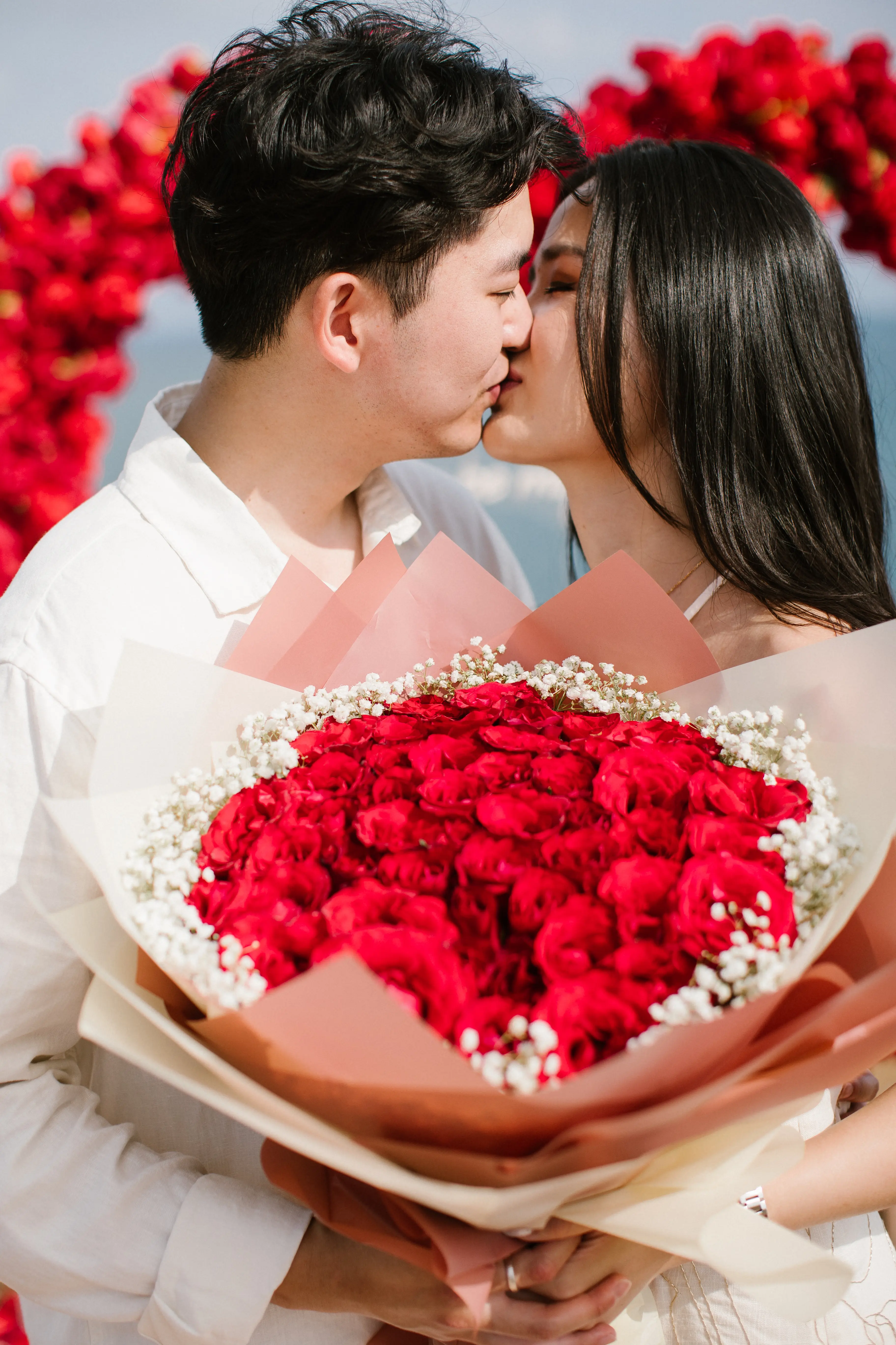 Couple just engaged on Bali cliff with red rose bouquet