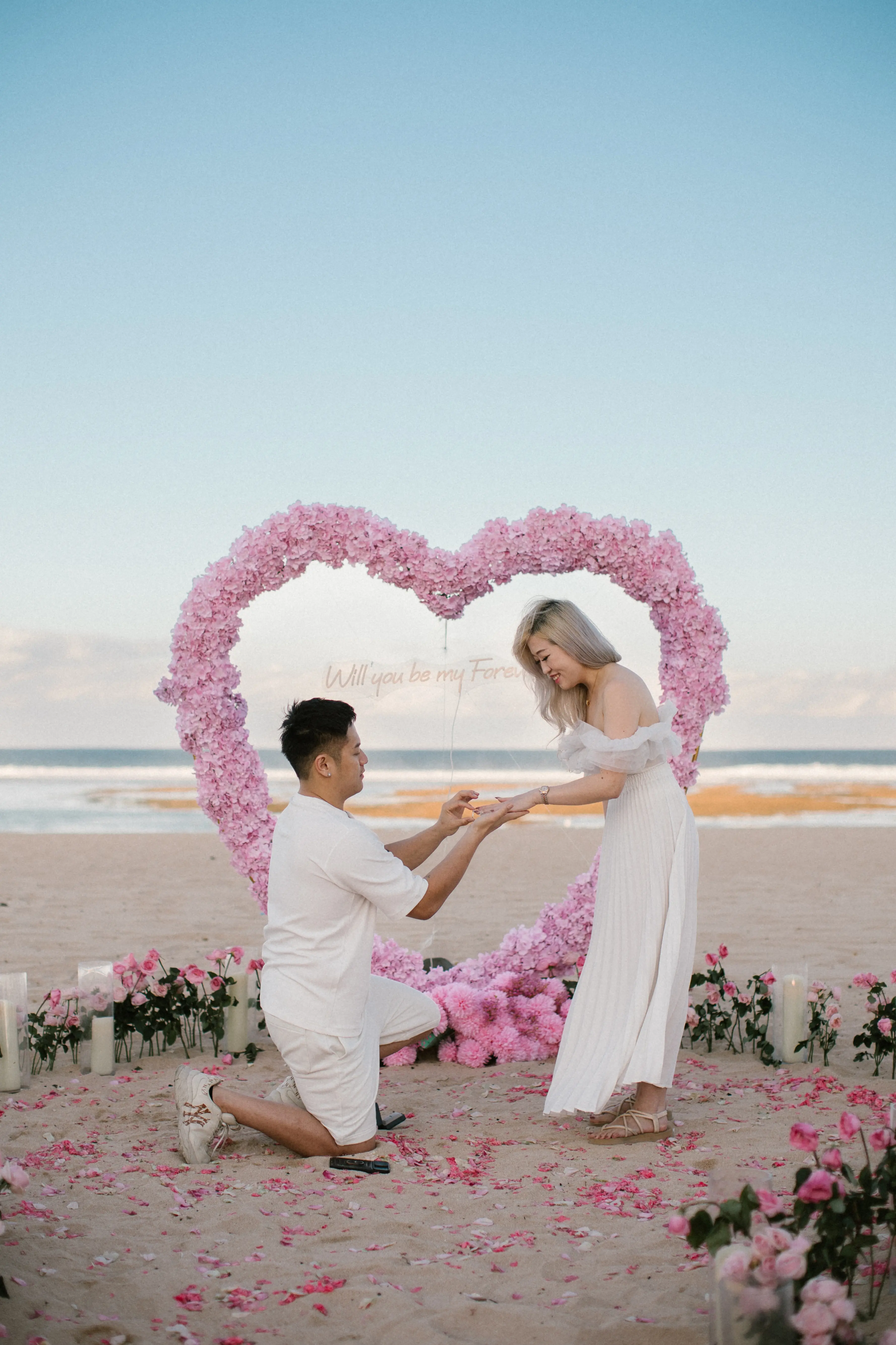 Couple engagement moment in Bali with floral heart arch on the beach