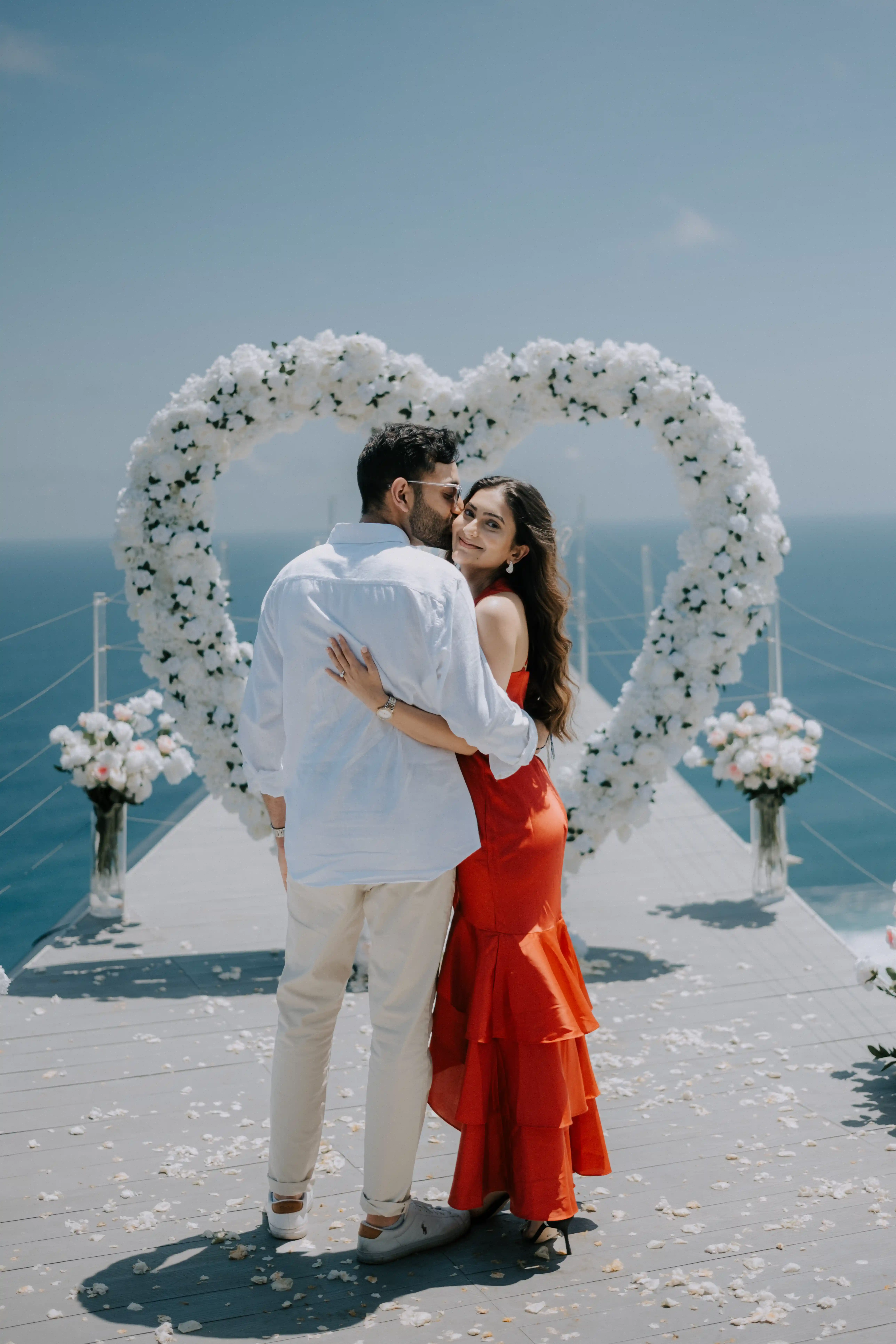Engagement kiss in Bali with flower arch and breathtaking cliff view.