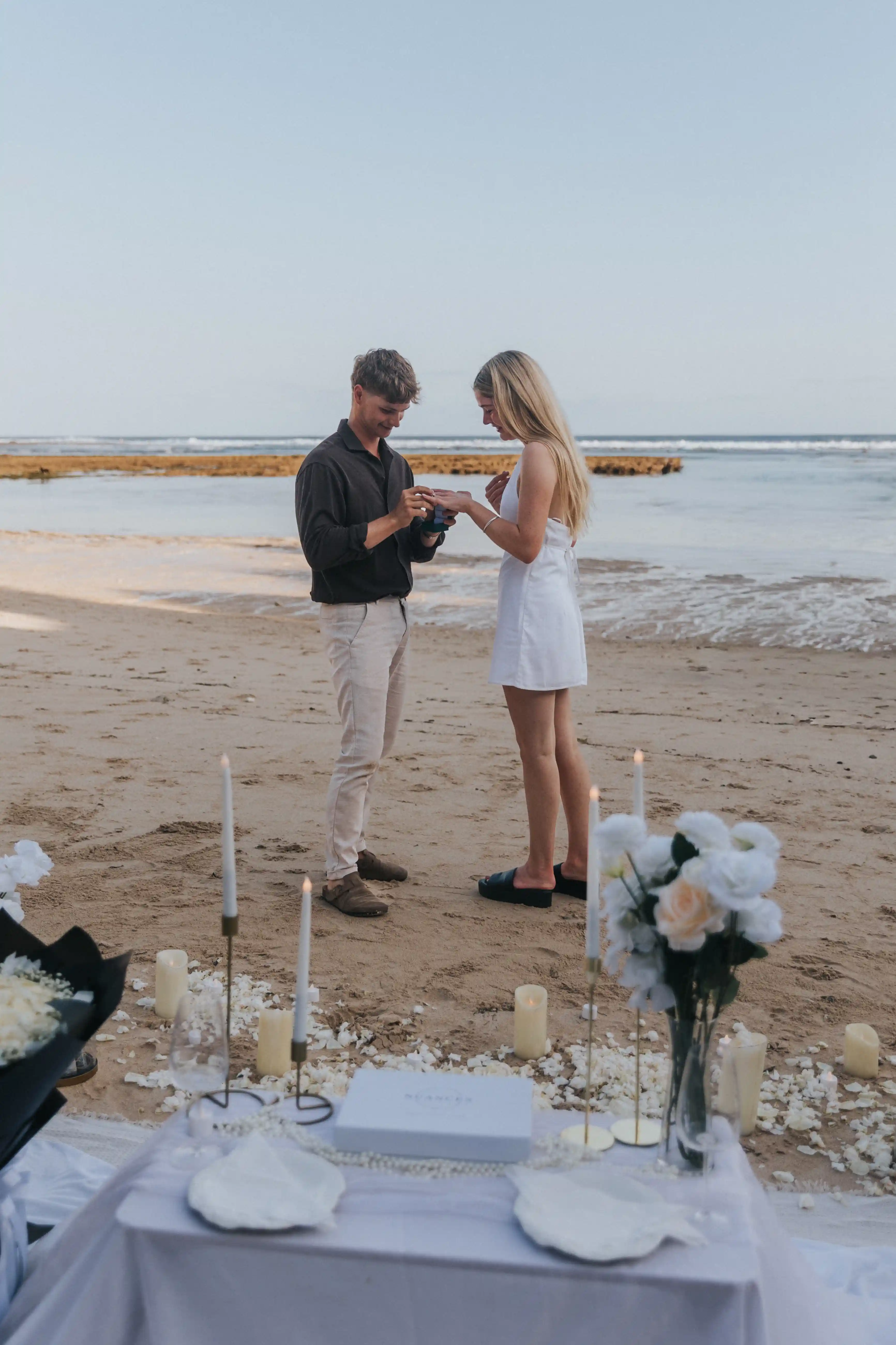 Elegant Bali proposal setup on the beach with white roses and candles.
