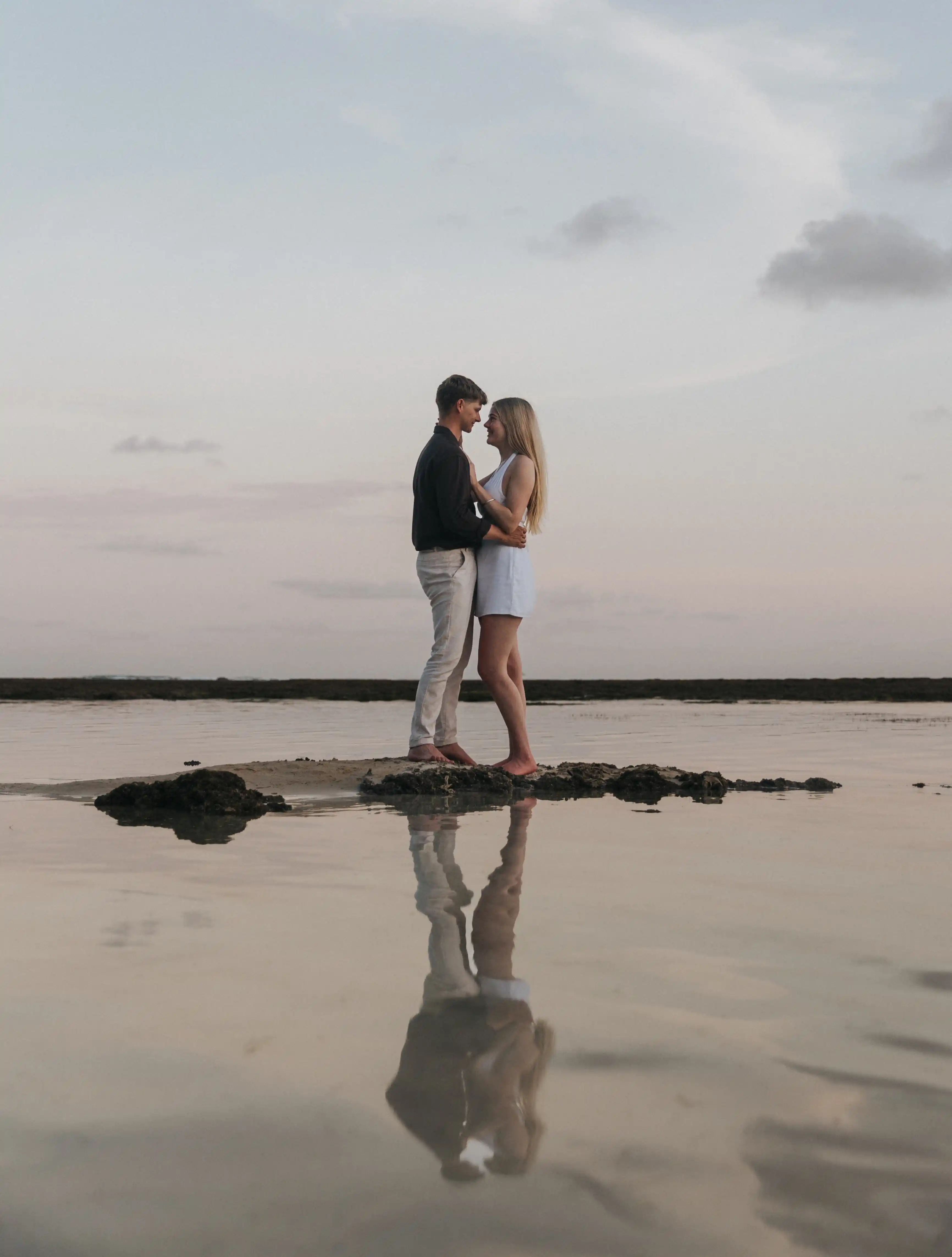 Couple enjoying a private engagement moment at their romantic Bali beach picnic setup during sunset.