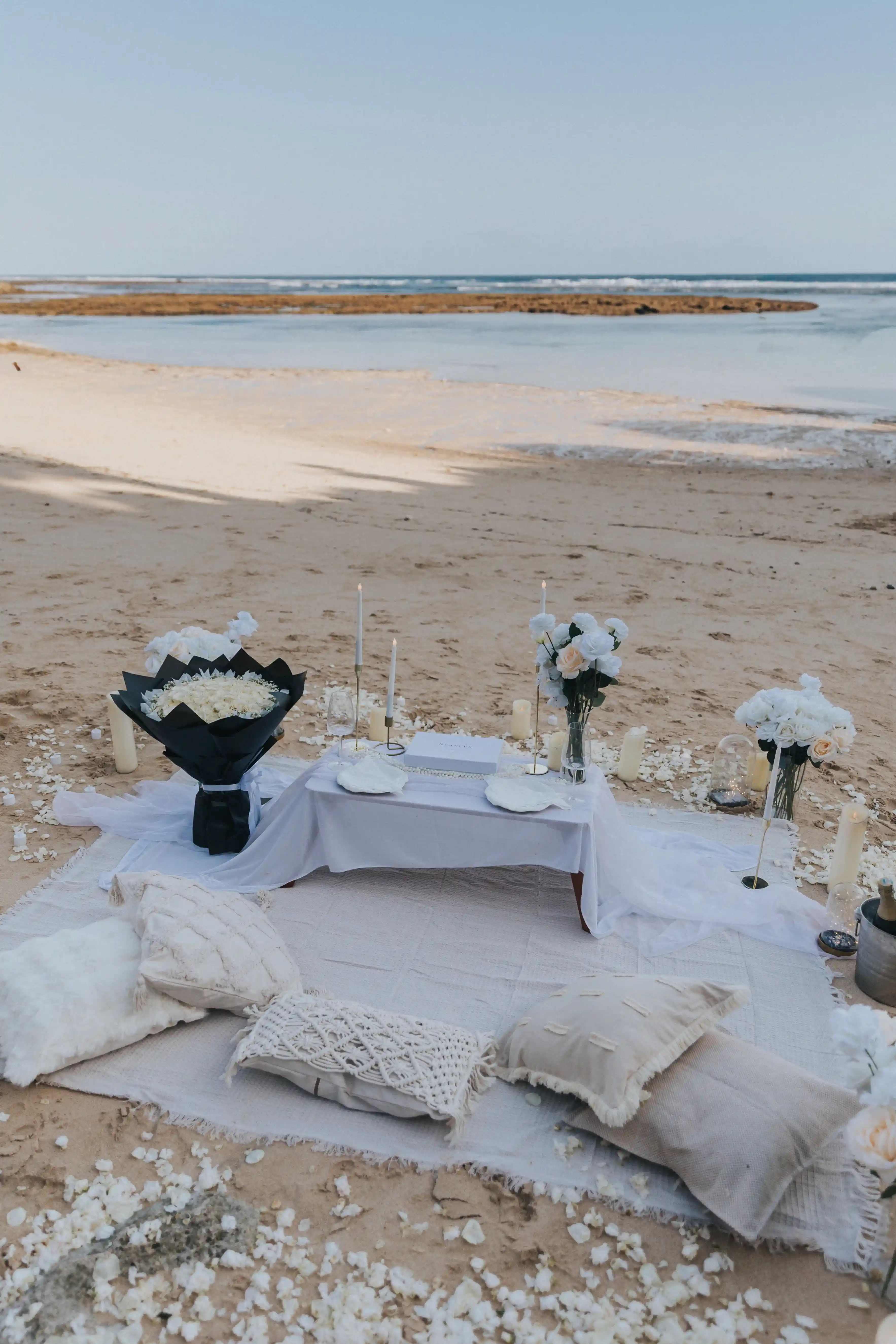 Romantic beach picnic setup in Bali with candles and white flowers.
