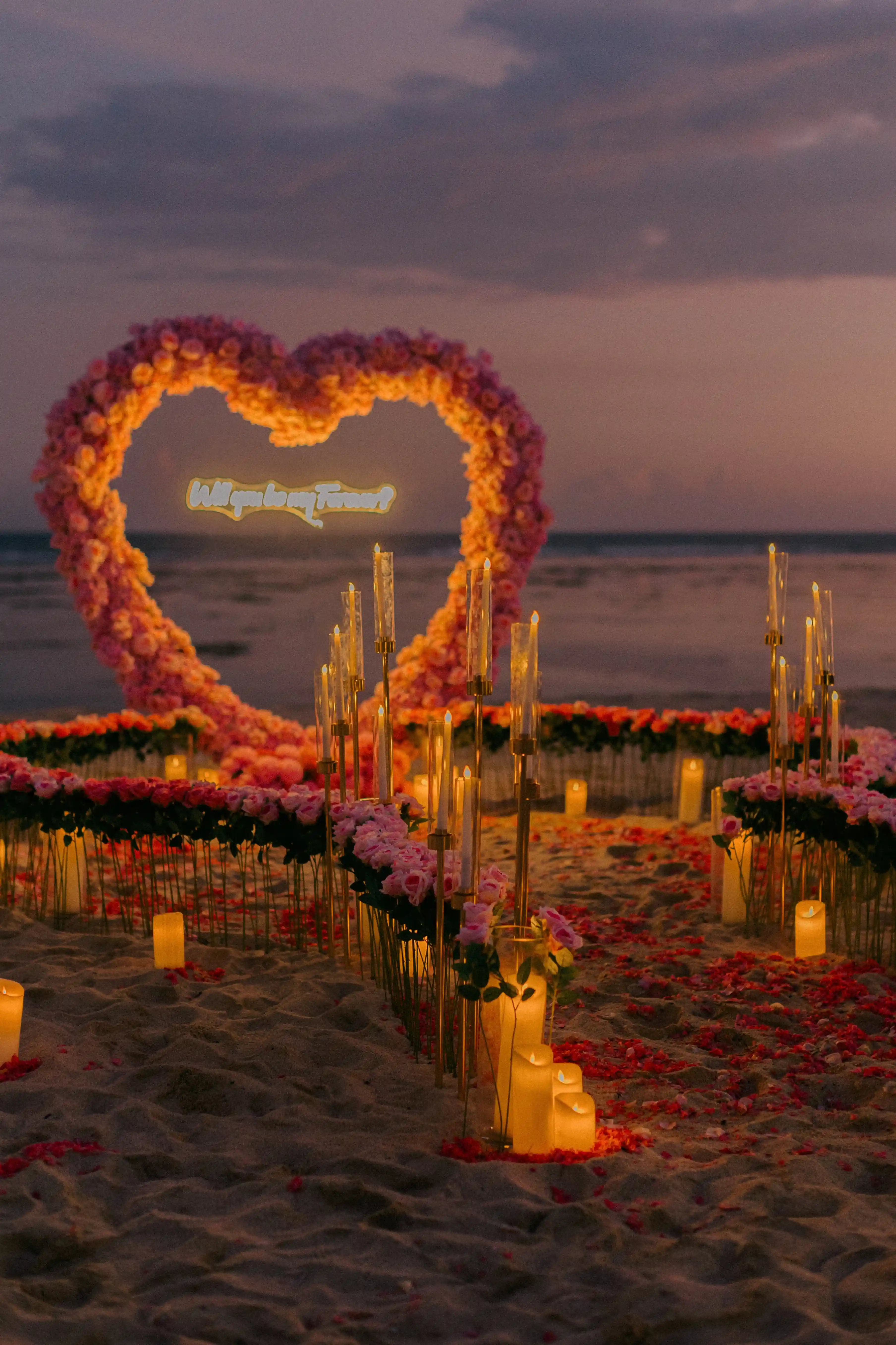 Heart arch illuminated at sunset during a Bali beach engagement setup.