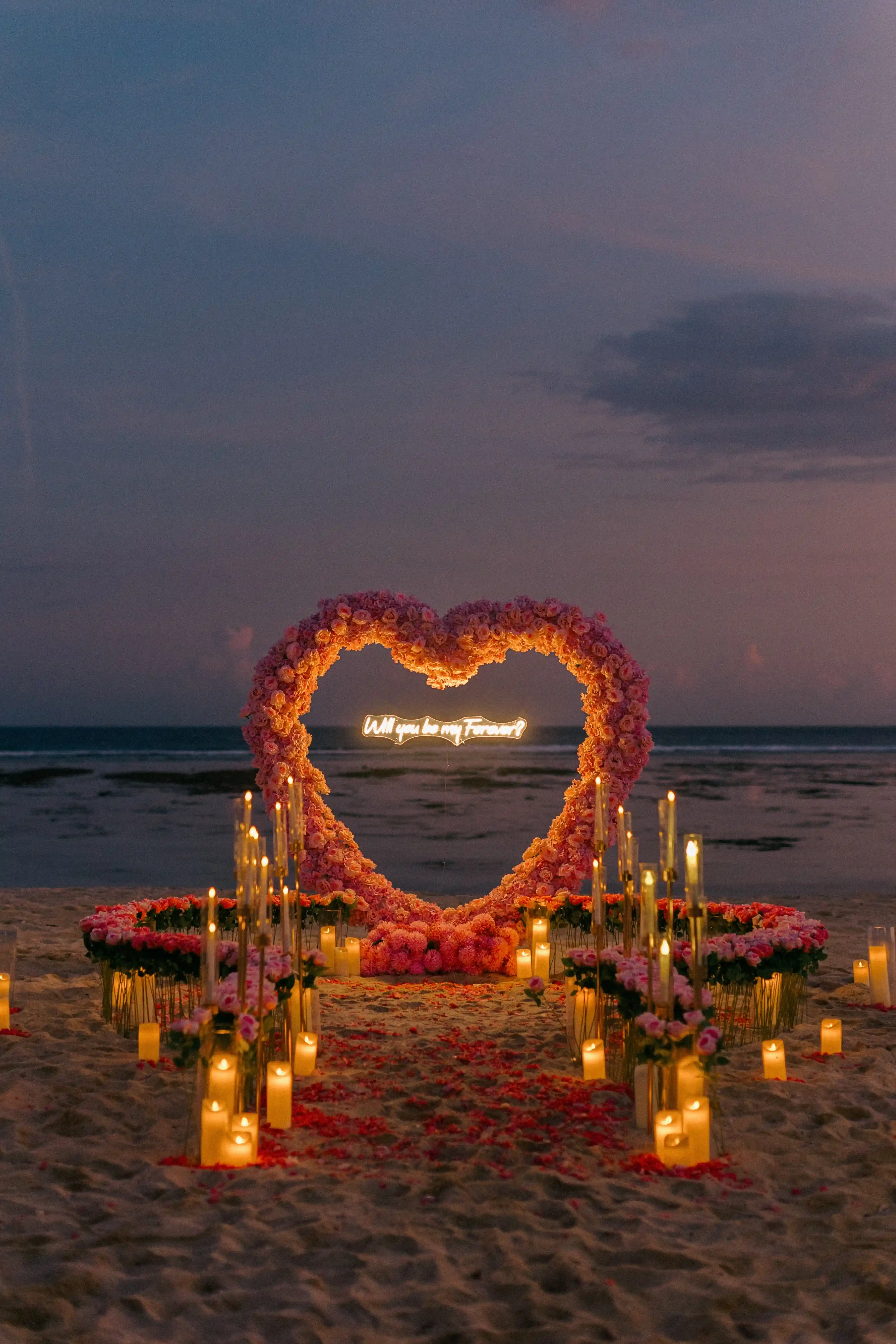 Romantic Bali proposal setup with glowing candles and pink floral heart arch.