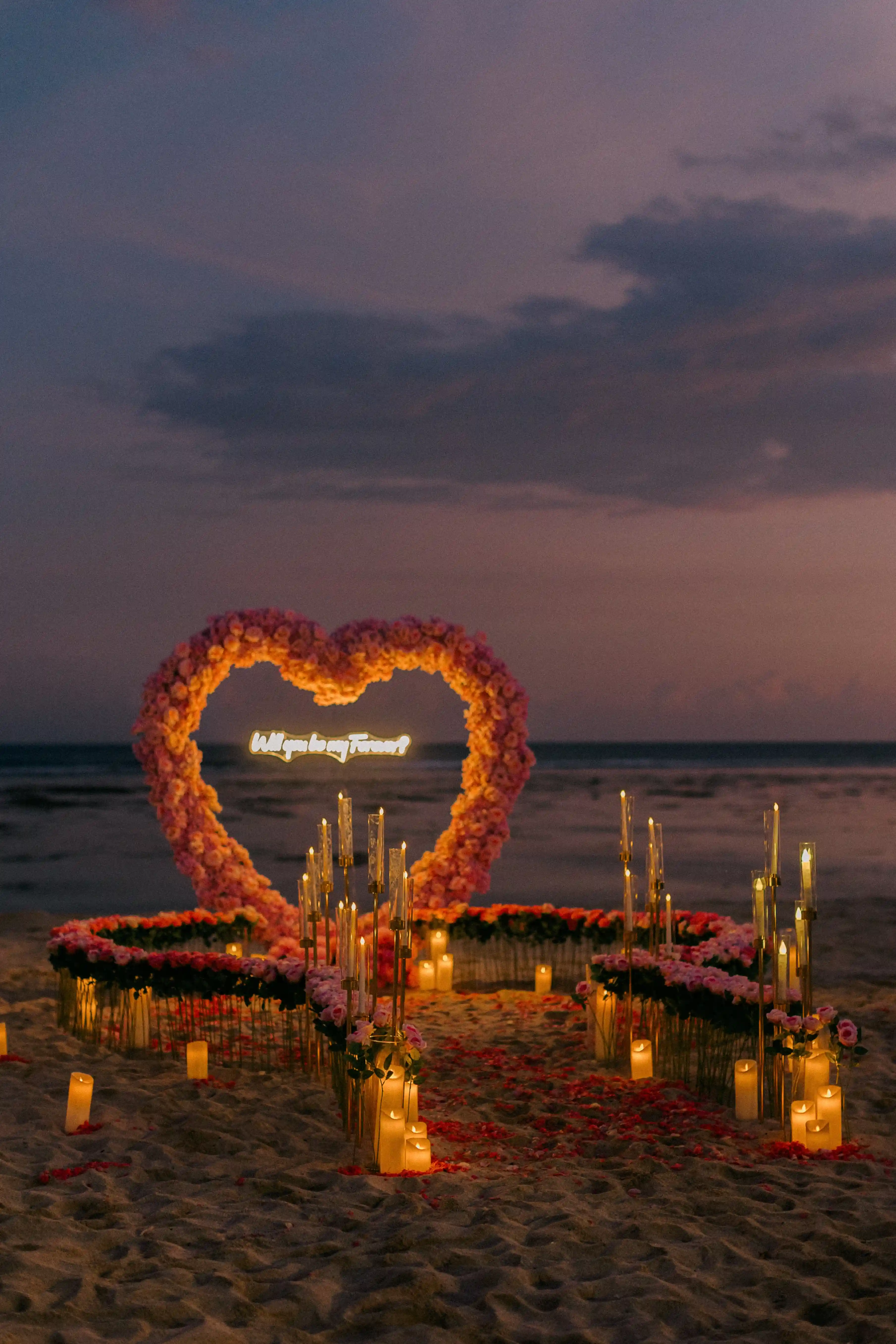 Dreamy beach engagement setup in Bali with candles, flowers, and ocean backdrop.