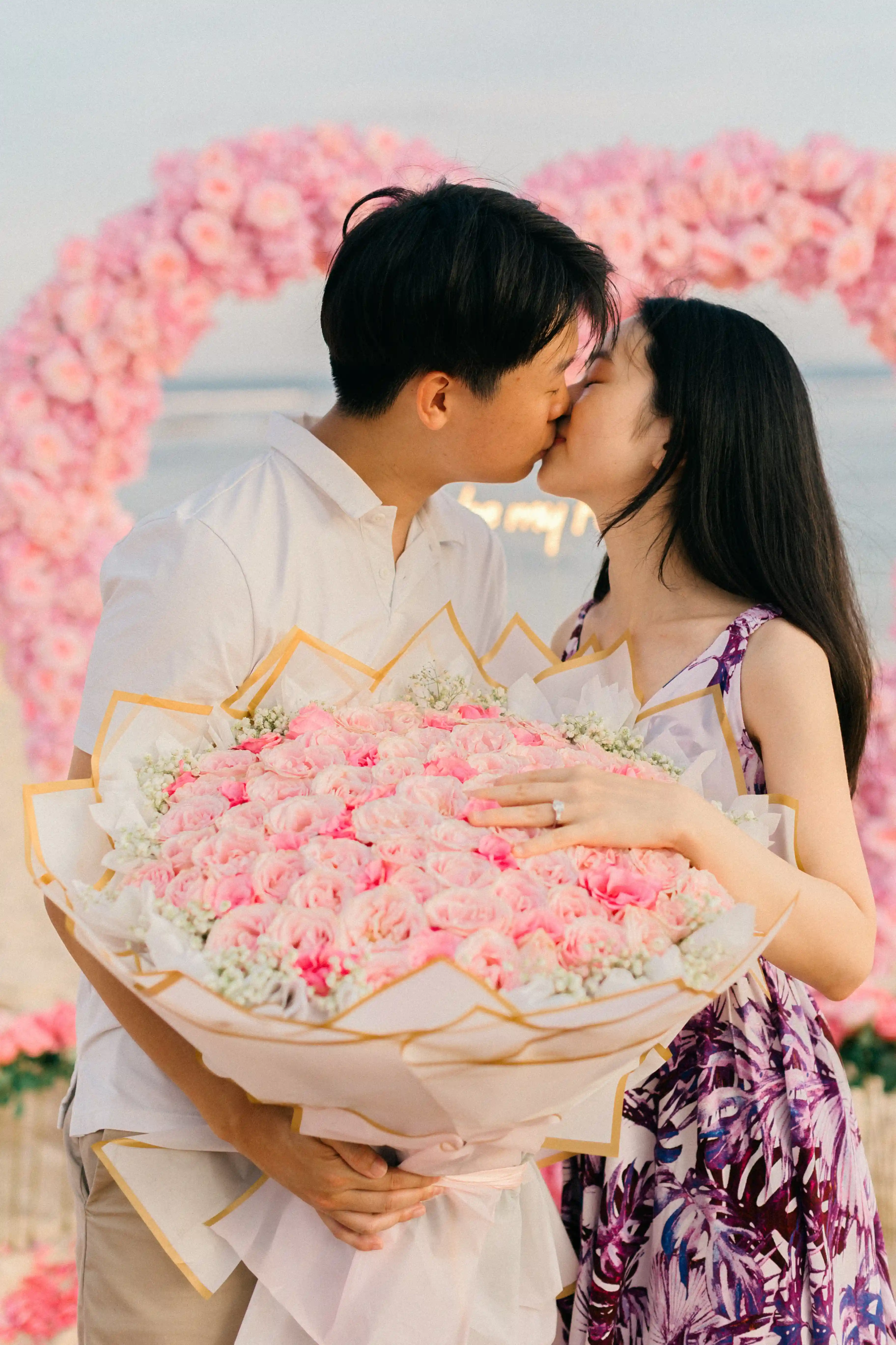 Couple kissing in front of a pink heart arch during Bali engagement.