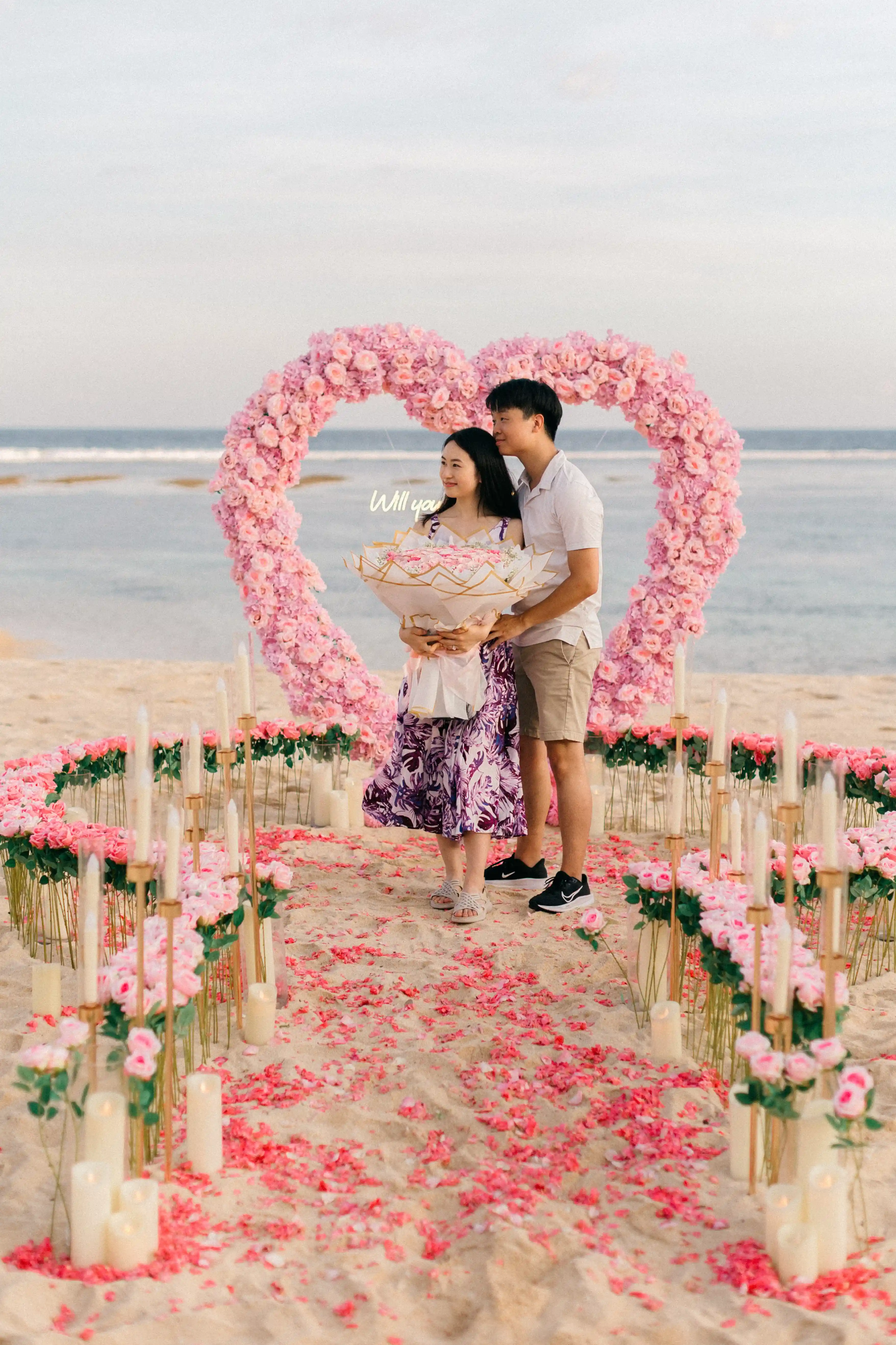 Beach proposal setup in Bali with flowers, candles, and sunset light.