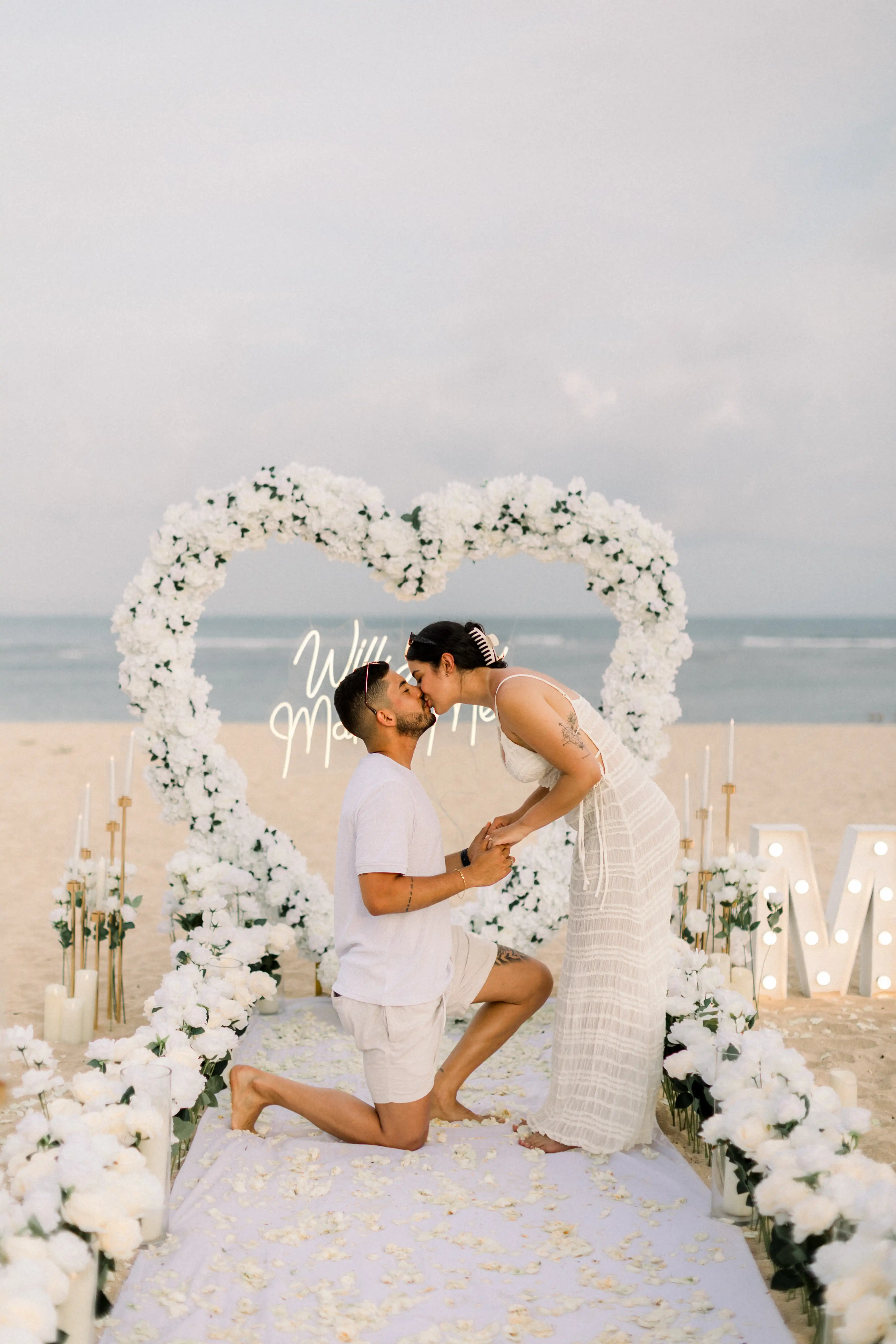 Elegant beach proposal setup in Bali featuring white flowers and candles.