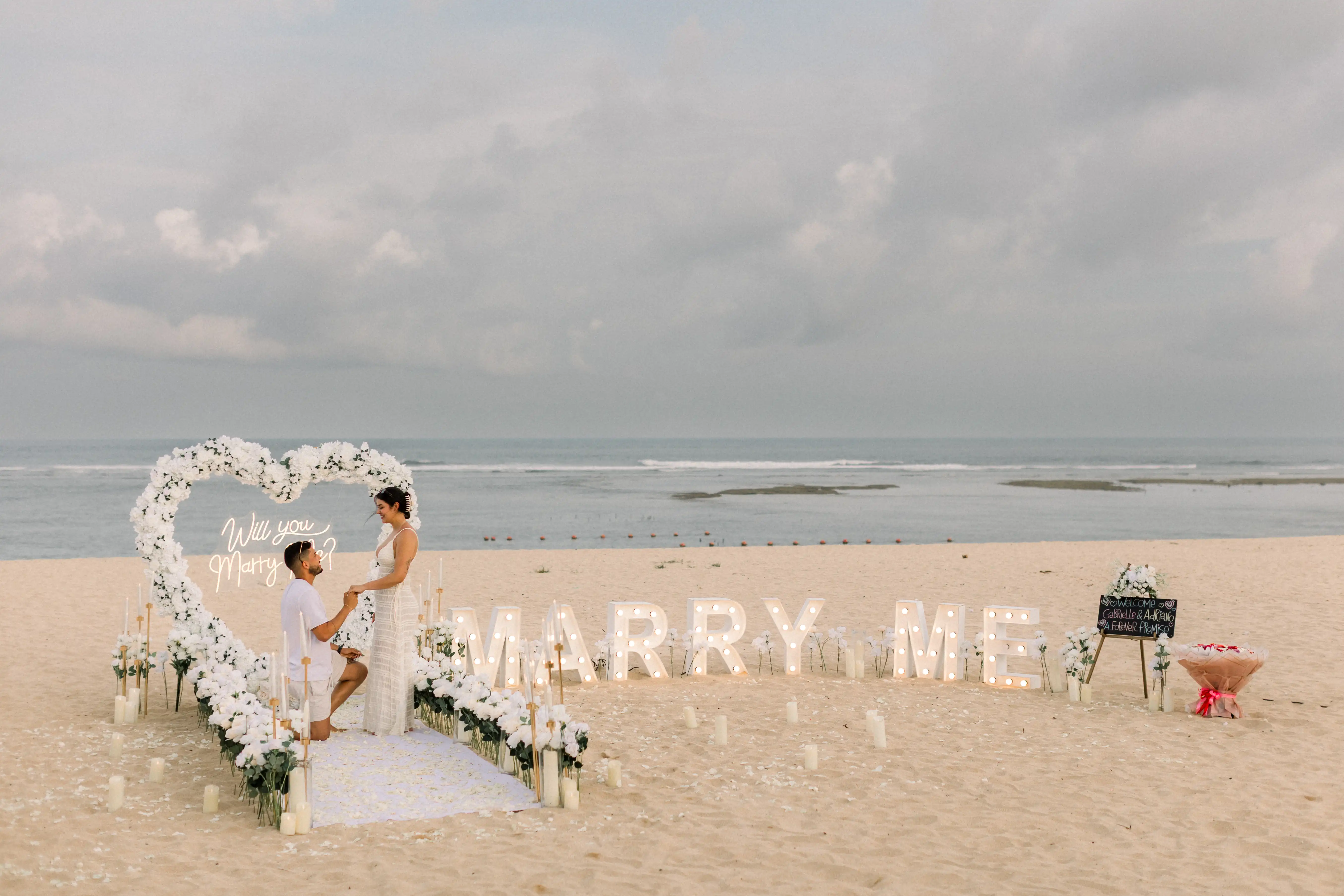 Romantic white and green floral beach proposal setup in Bali.