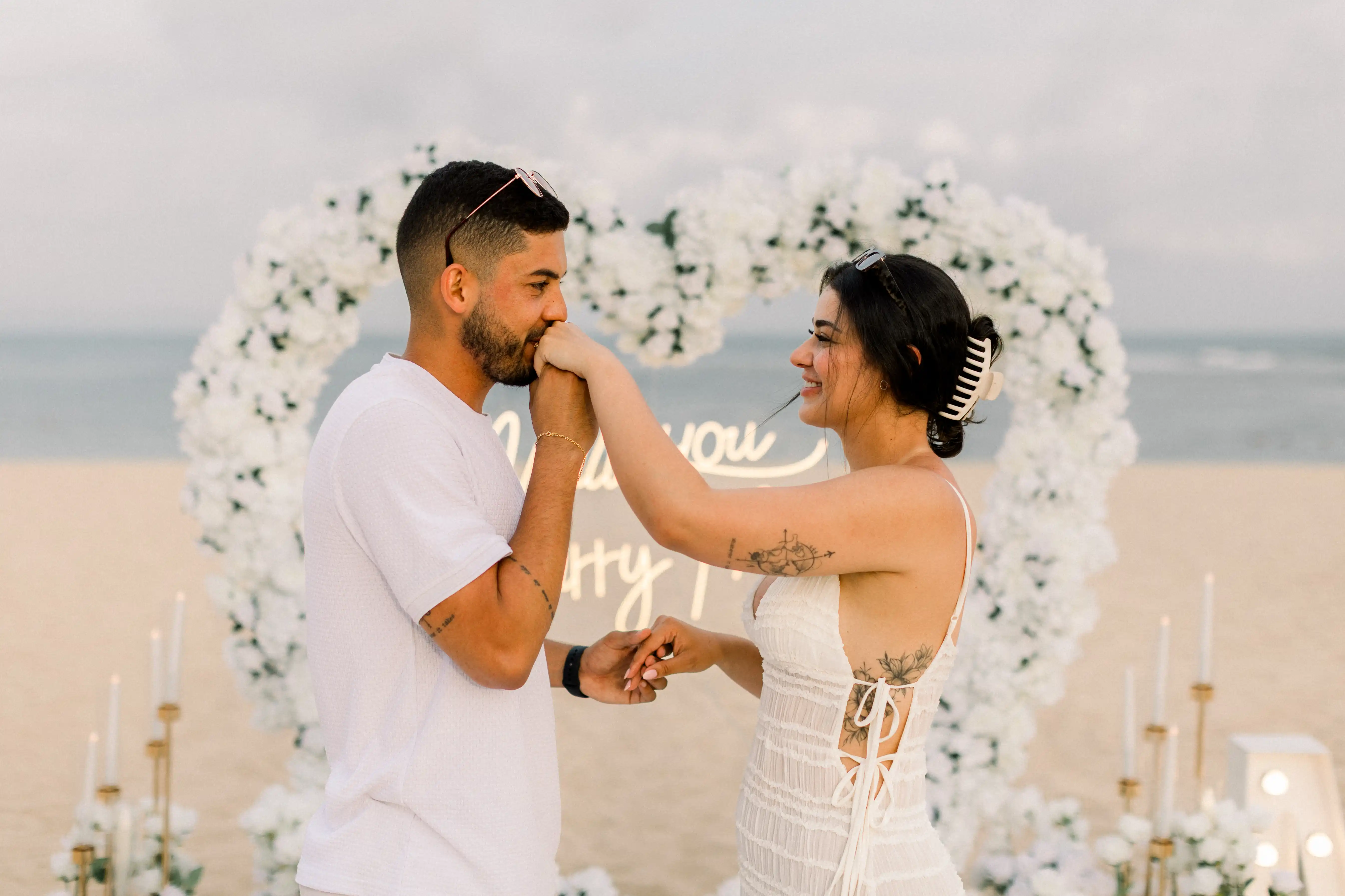 Happy couple celebrating engagement in front of white heart arch in Bali.
