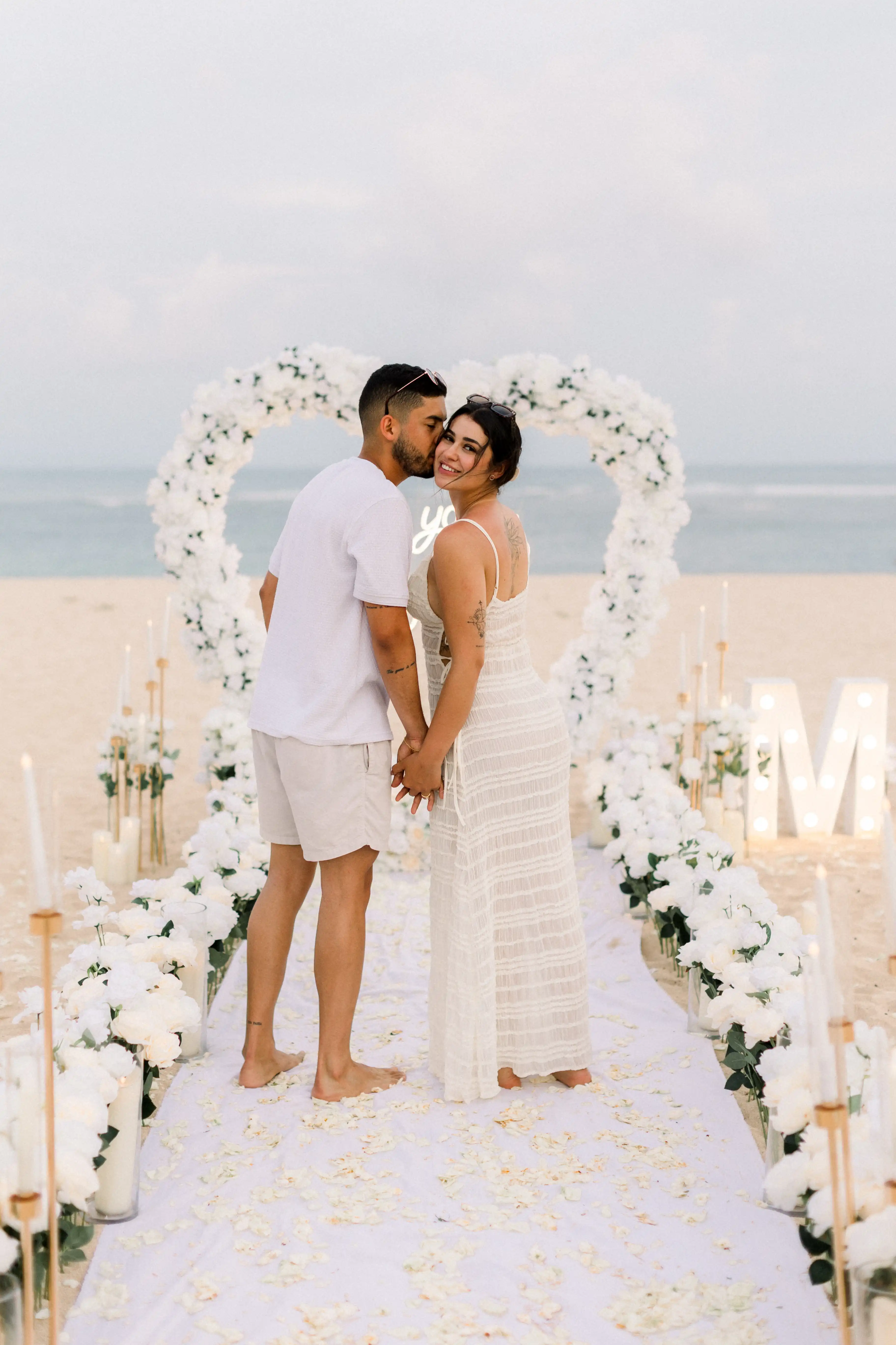 Romantic Bali proposal scene with heart arch, candles, and “Marry Me” sign.