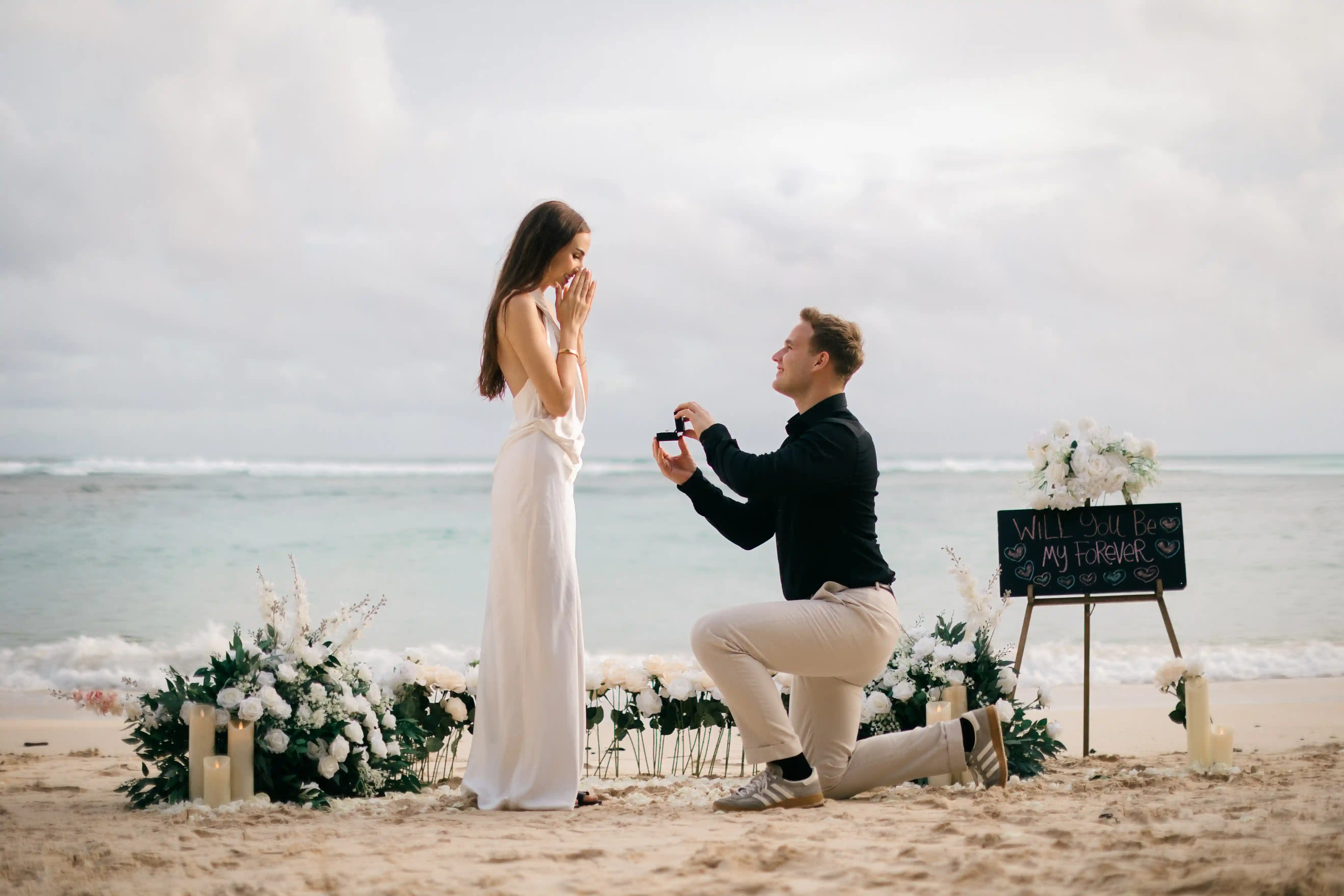 Lucas proposing on one knee in a minimalist beach setup by the sea.