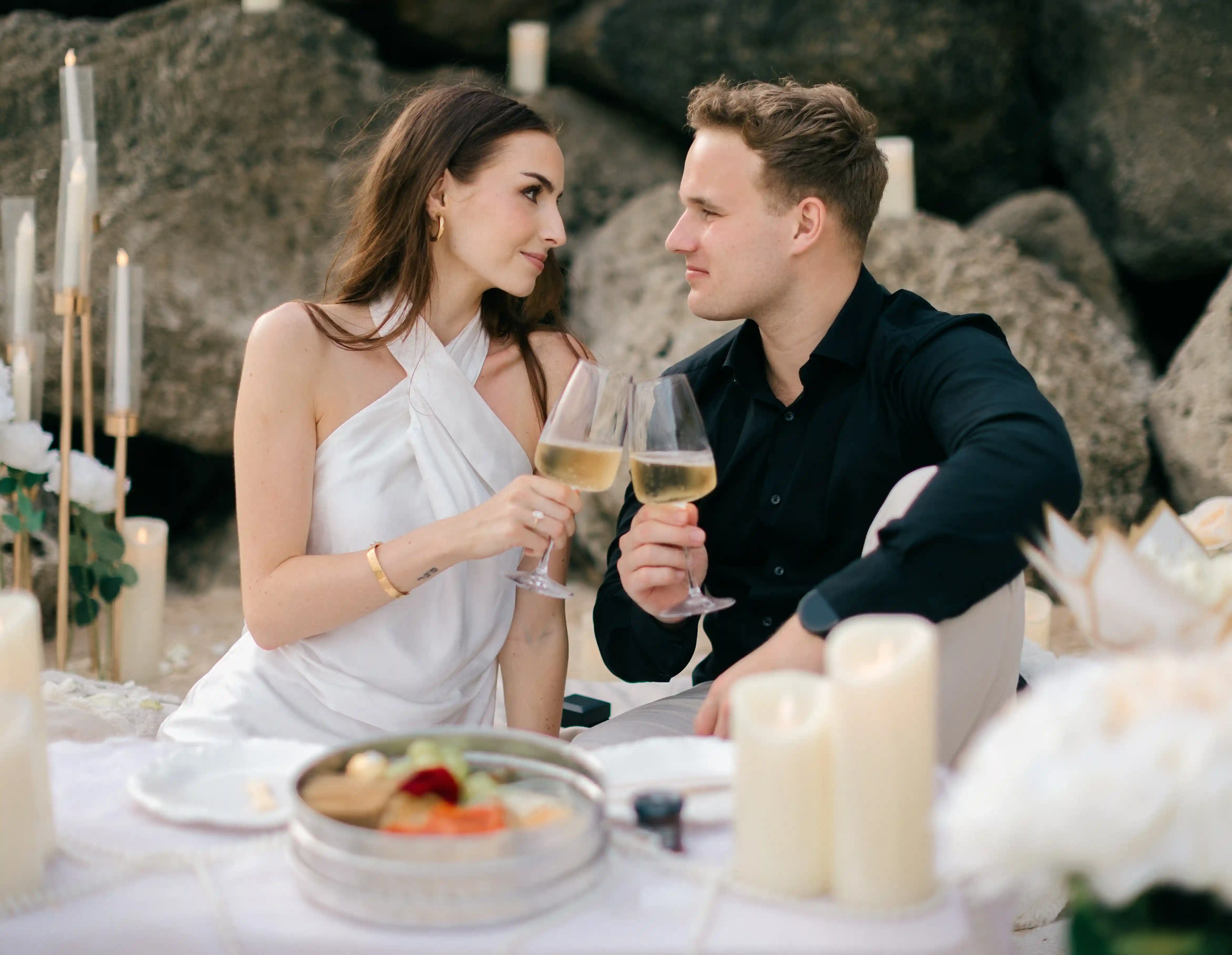 The couple enjoying their styled beach picnic with champagne and candles.