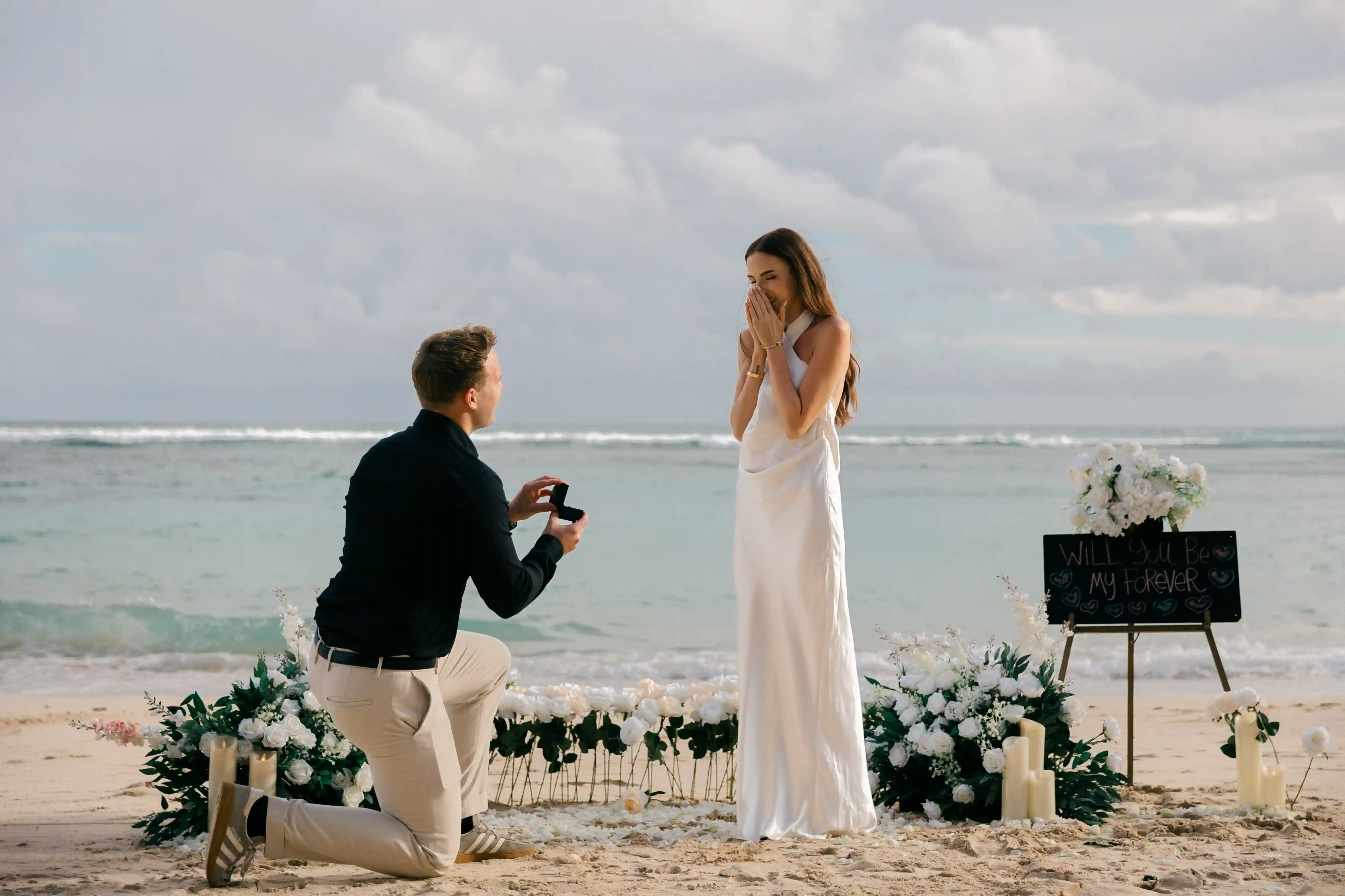 Lucas on one knee asking Jasmin to marry him with the ocean behind them.