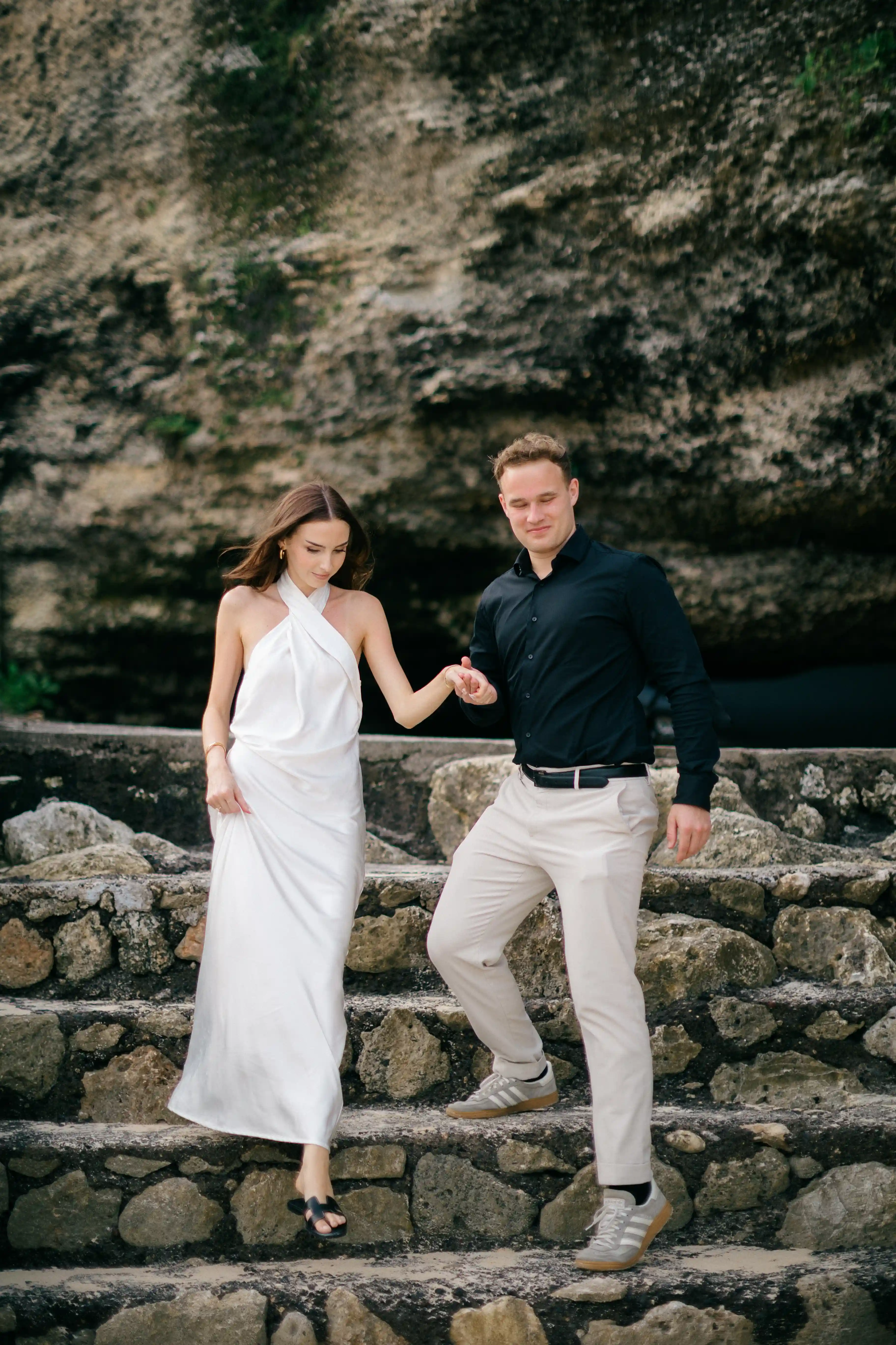 Jasmin and Lucas walking together along the rocky beach landscape in Bali.