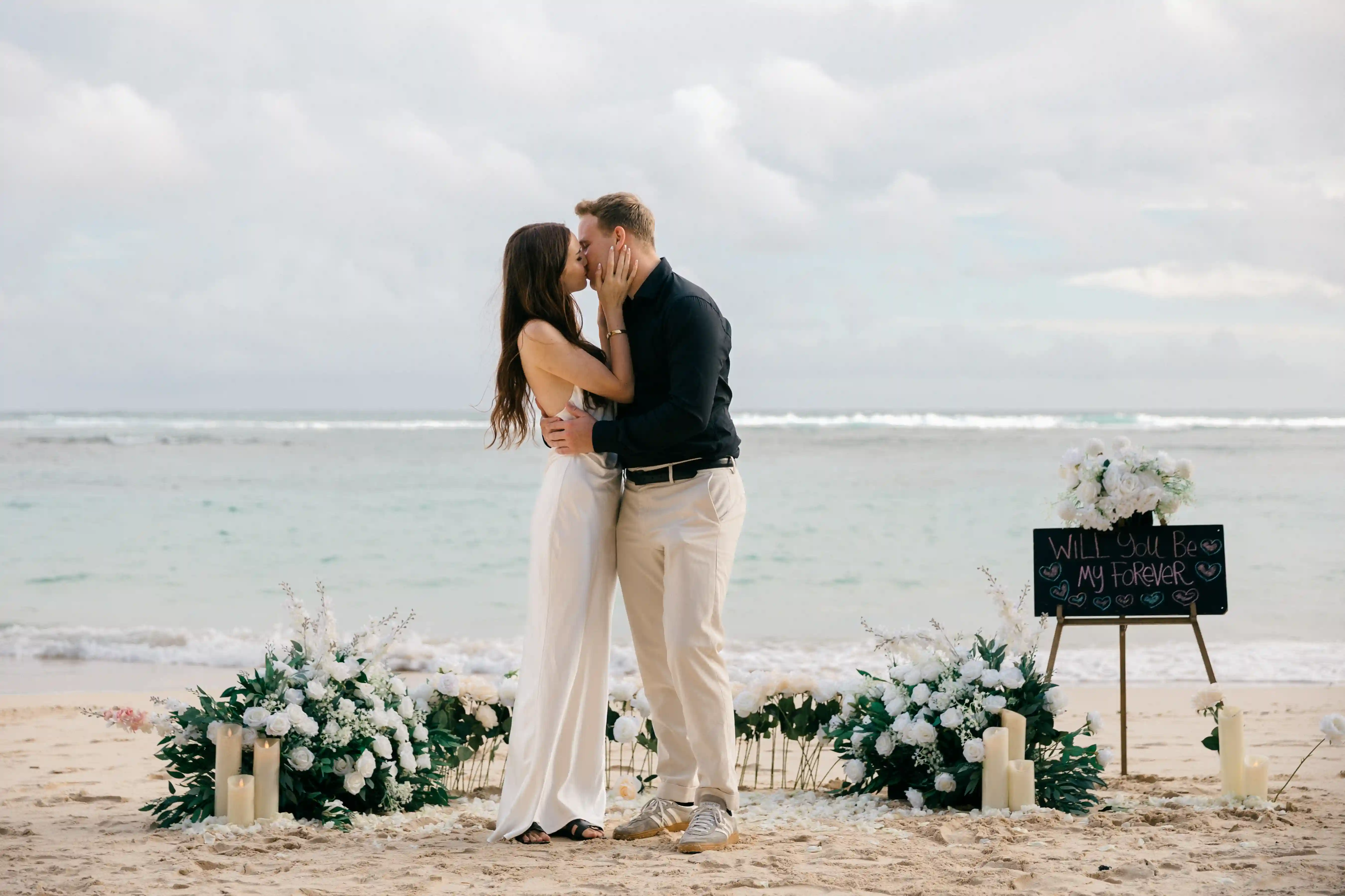 Emotional kiss right after she said yes, framed by the beach setup.