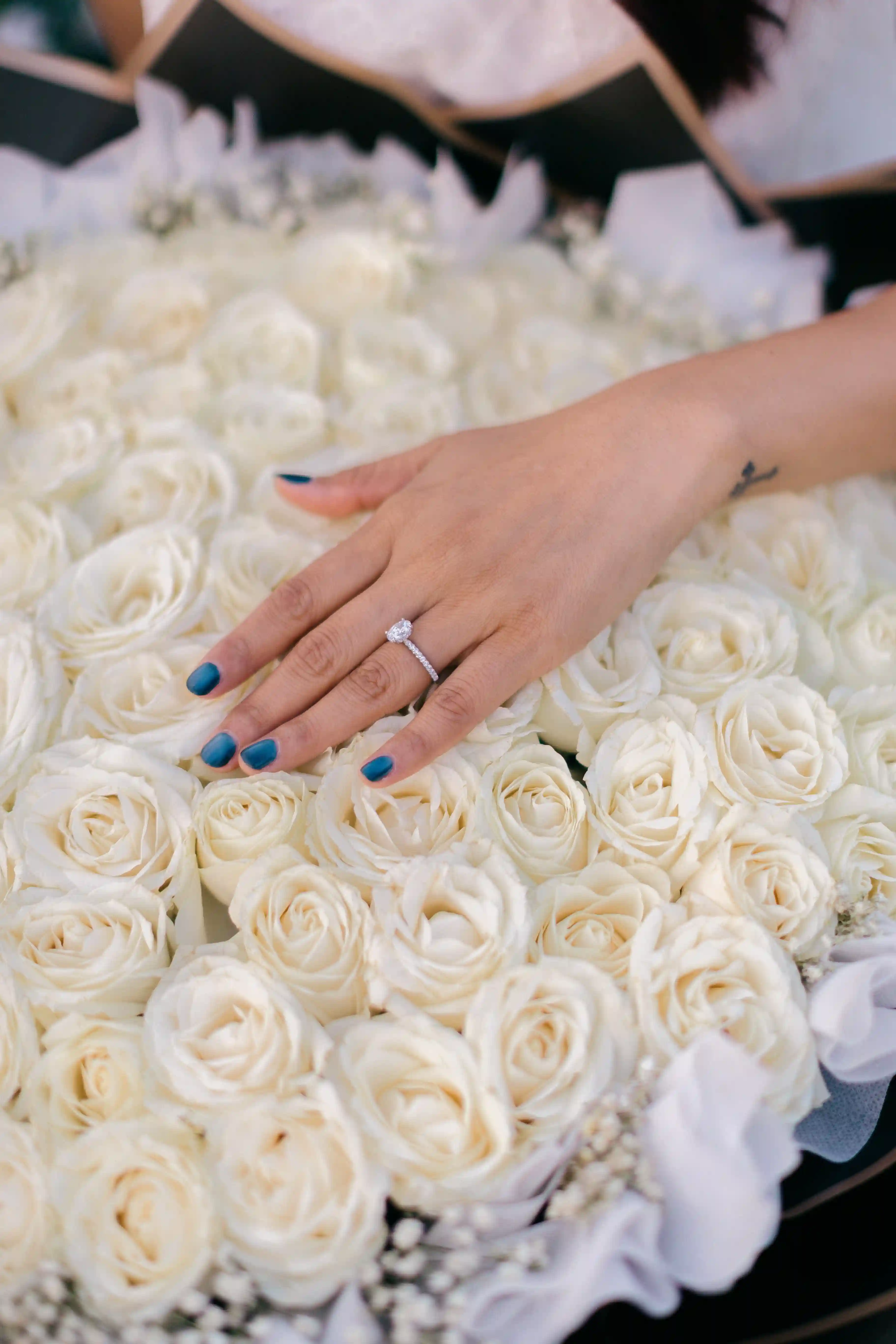 Close-up of engagement ring on hand over white roses