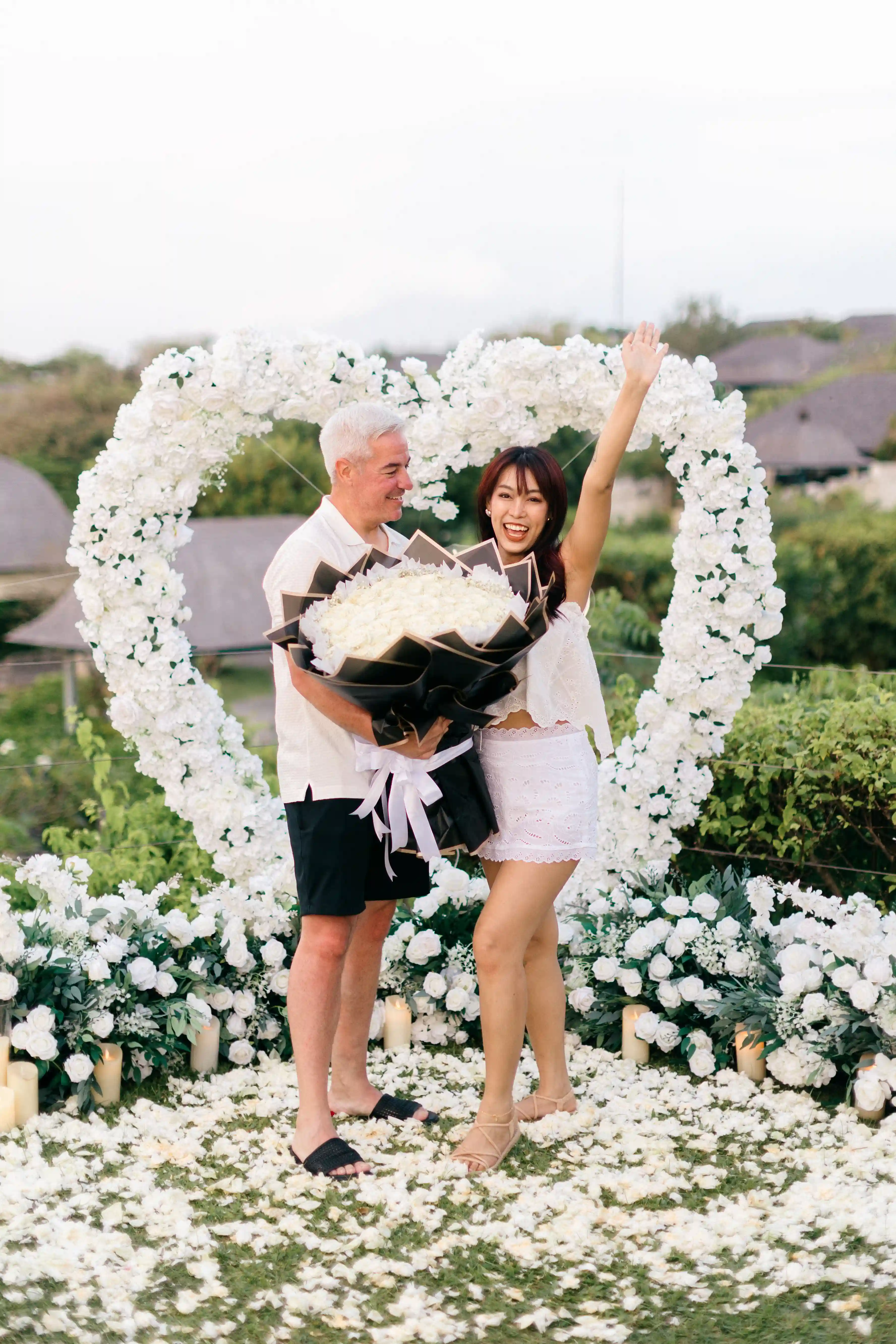 Couple celebrating engagement in front of floral arch with flowers