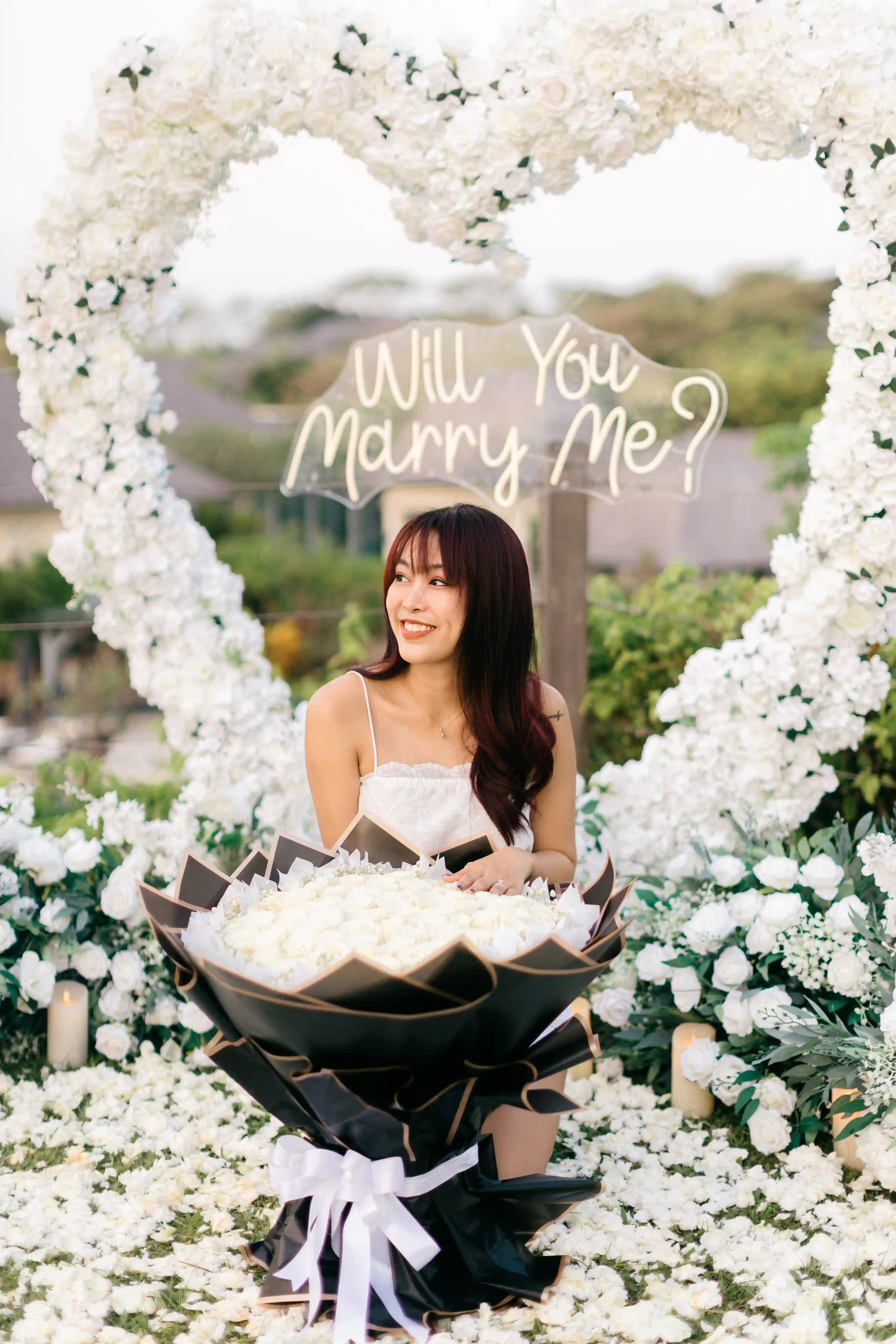 Woman standing in front of floral heart arch holding bouquet