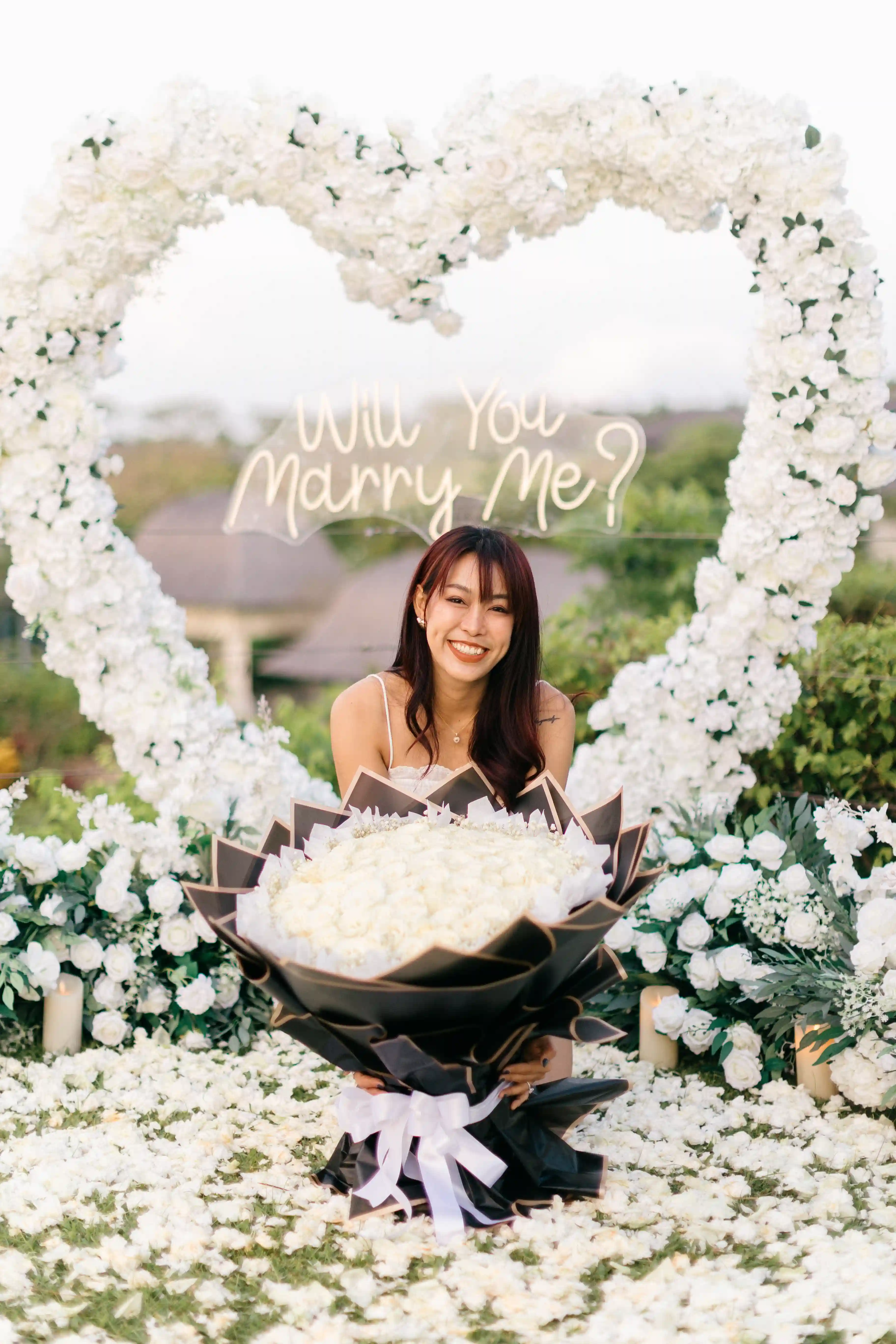 Woman holding bouquet in front of heart-shaped floral arch in Bali