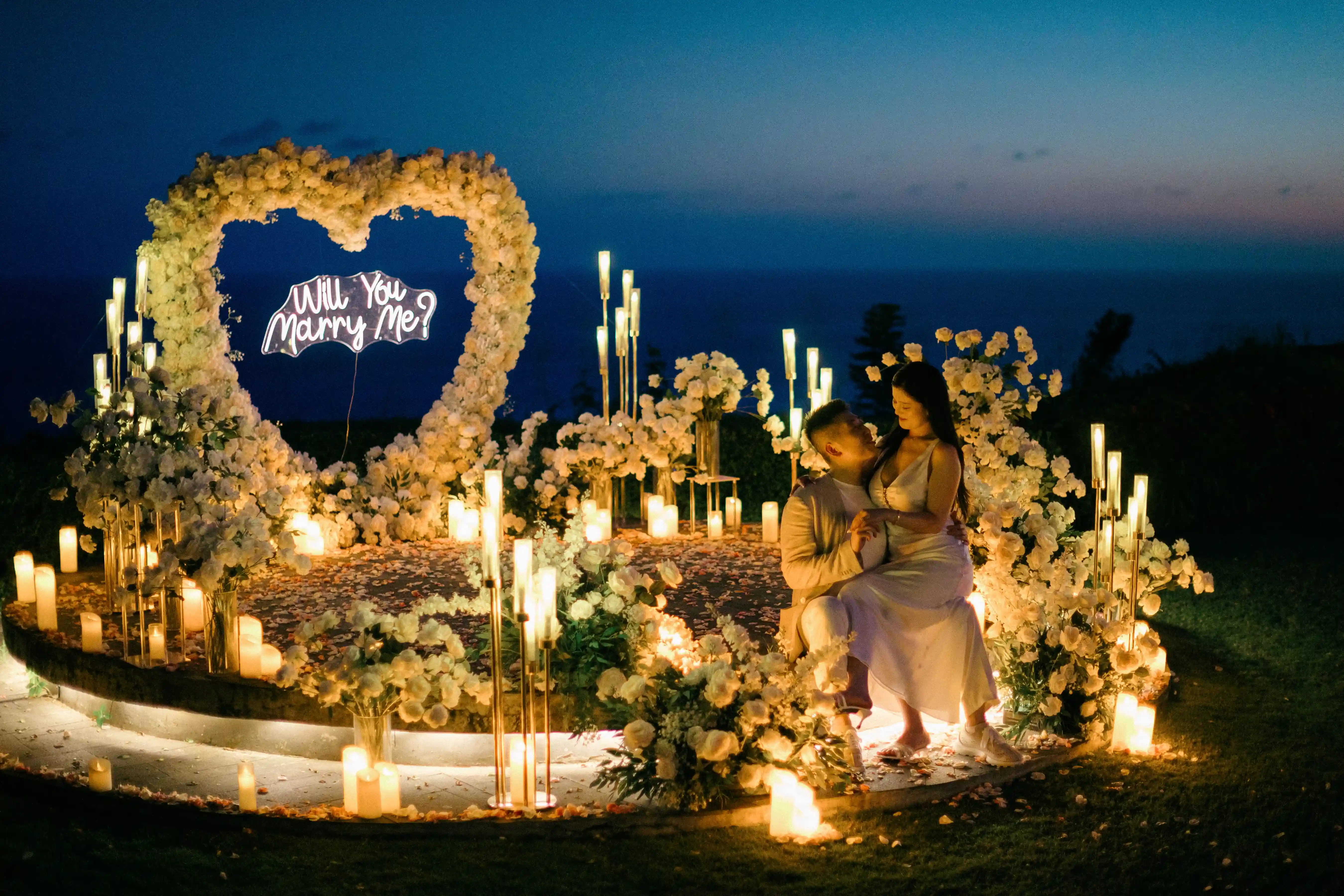 Romantic cliffside proposal setup in Bali with heart arch and candlelight at sunset