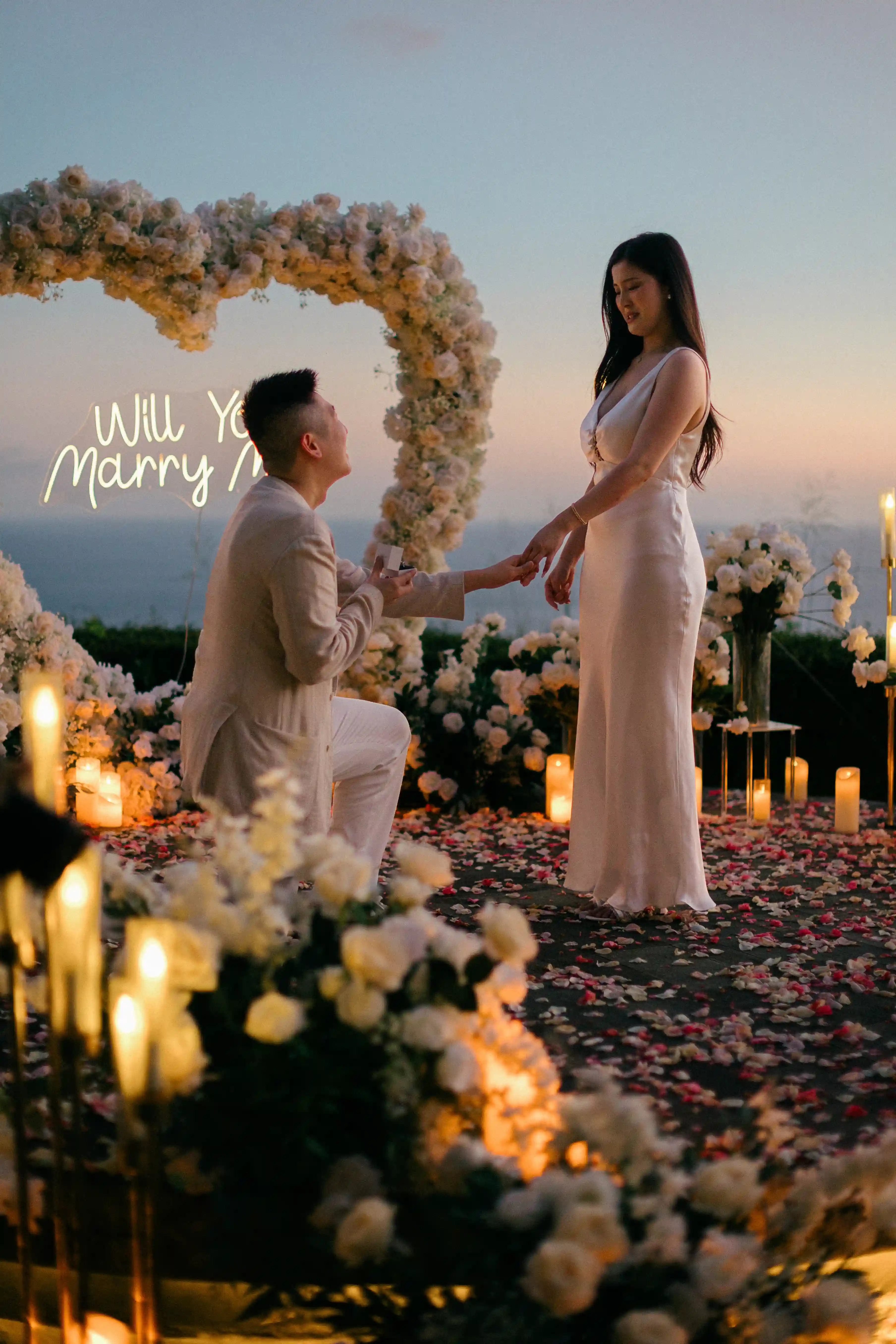 Man proposing under a floral heart arch at sunset in Bali