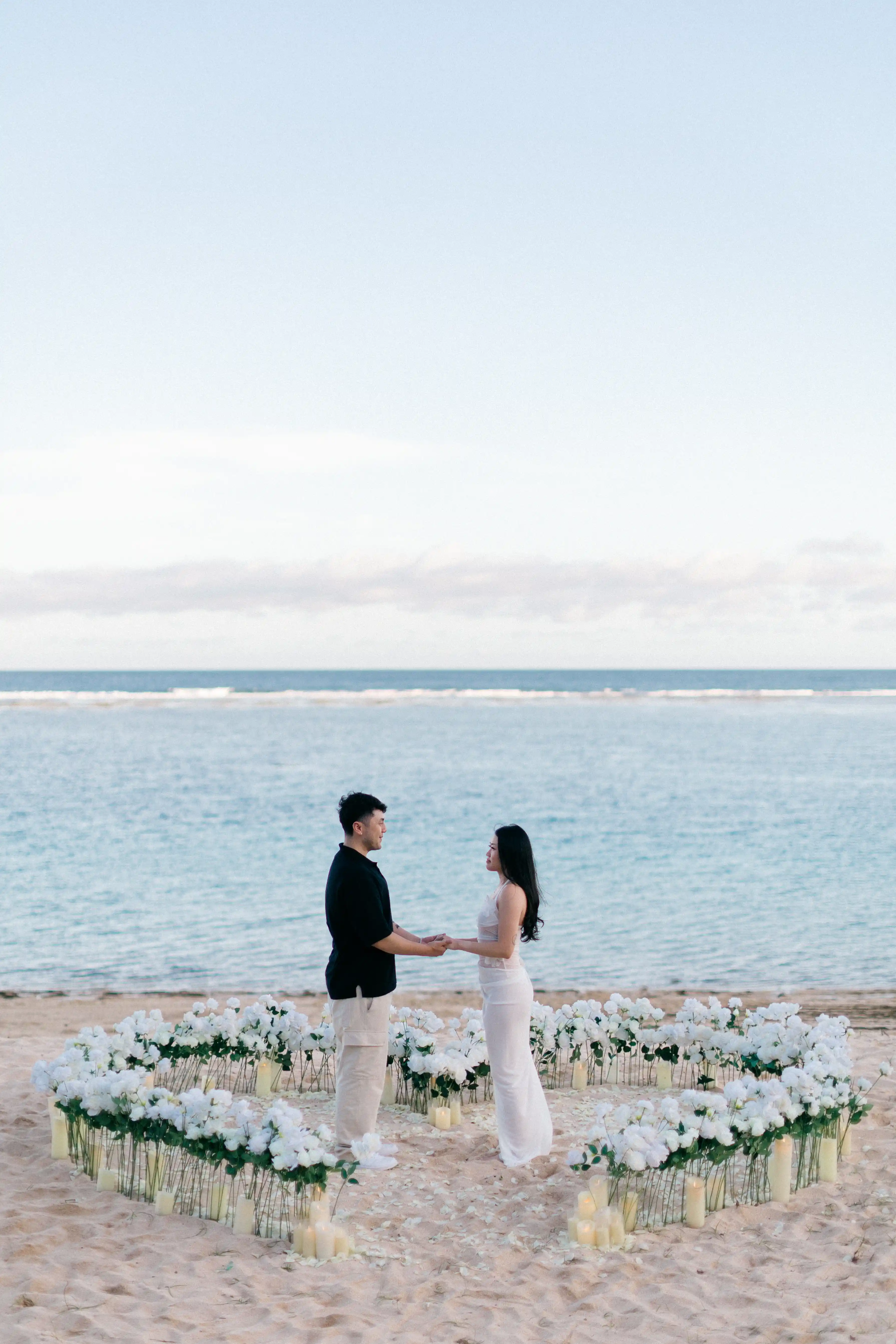 Couple standing inside rose heart arrangement during beach proposal in Bali