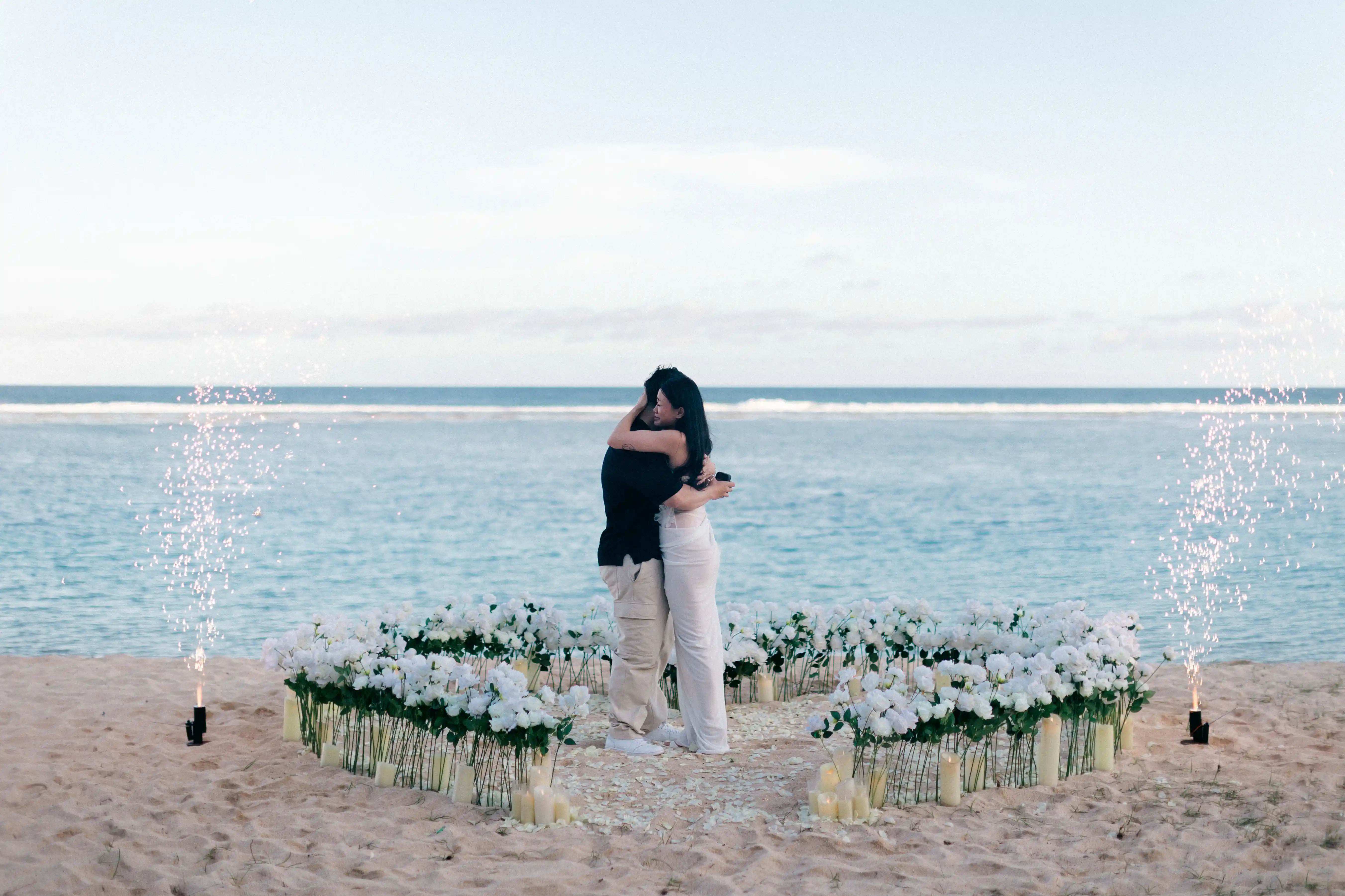 Couple embracing inside heart-shaped rose arrangement on the beach