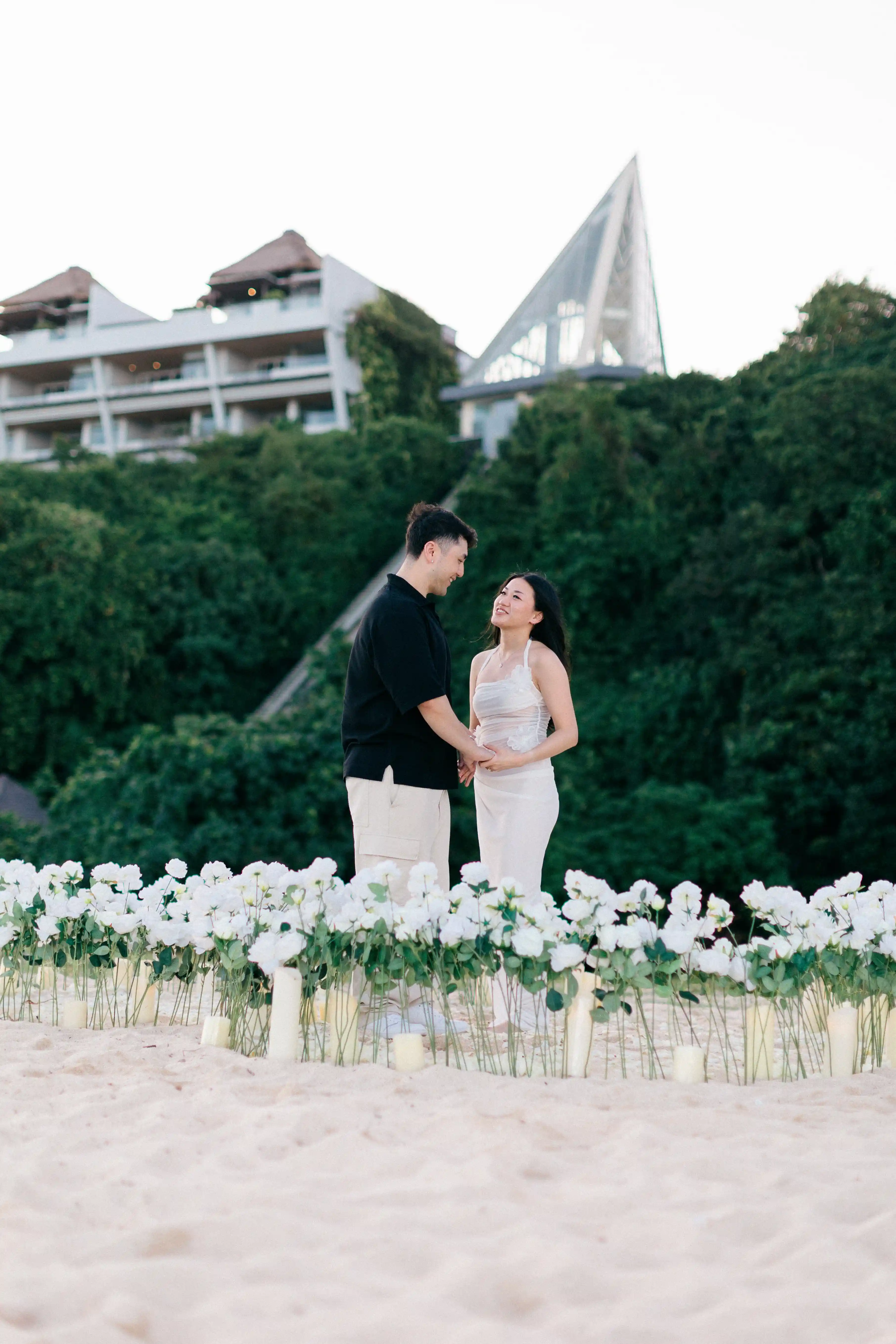 Couple standing at luxury beach proposal setup with floral arrangements