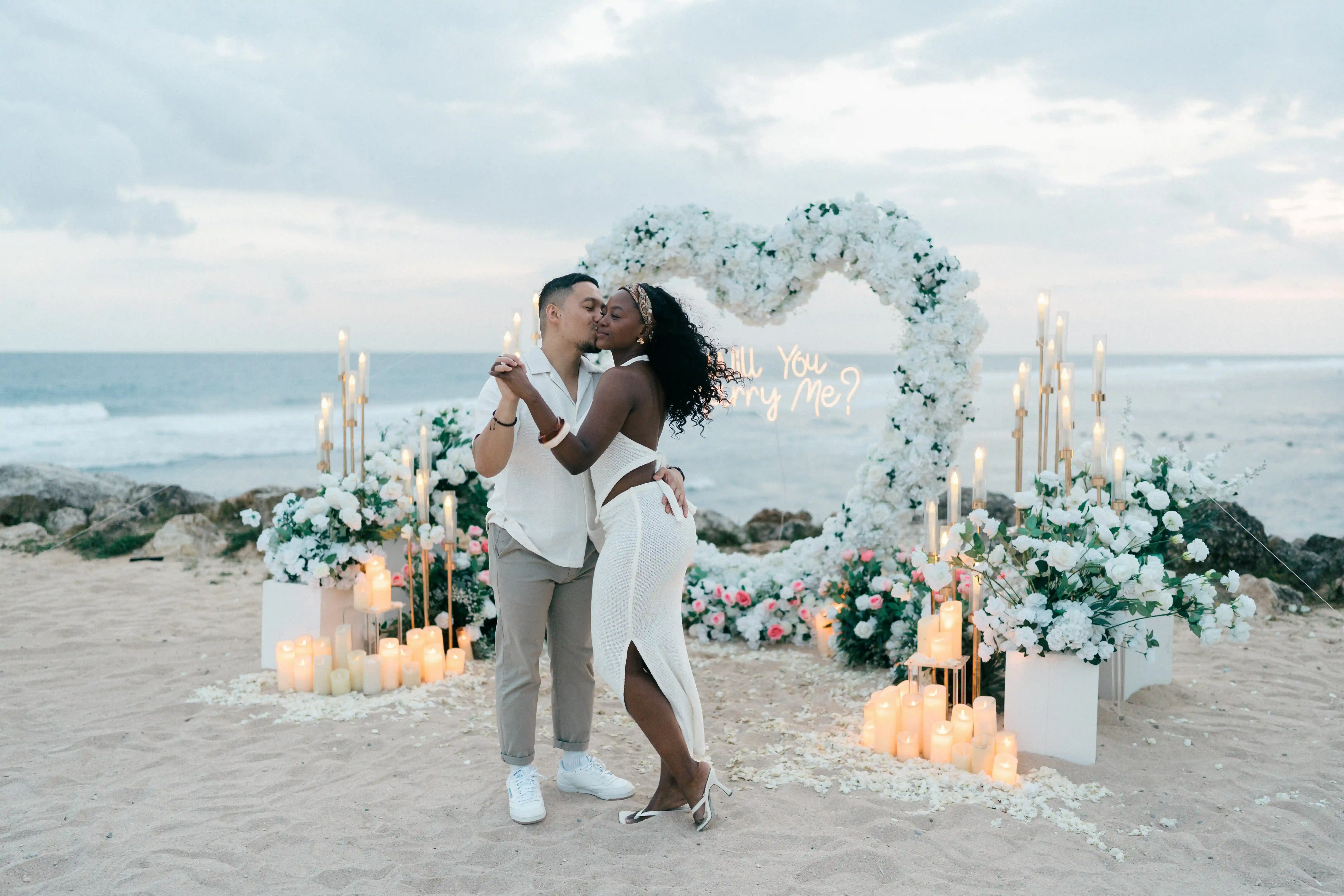 Engaged couple celebrating at cliffside proposal setup overlooking the ocean