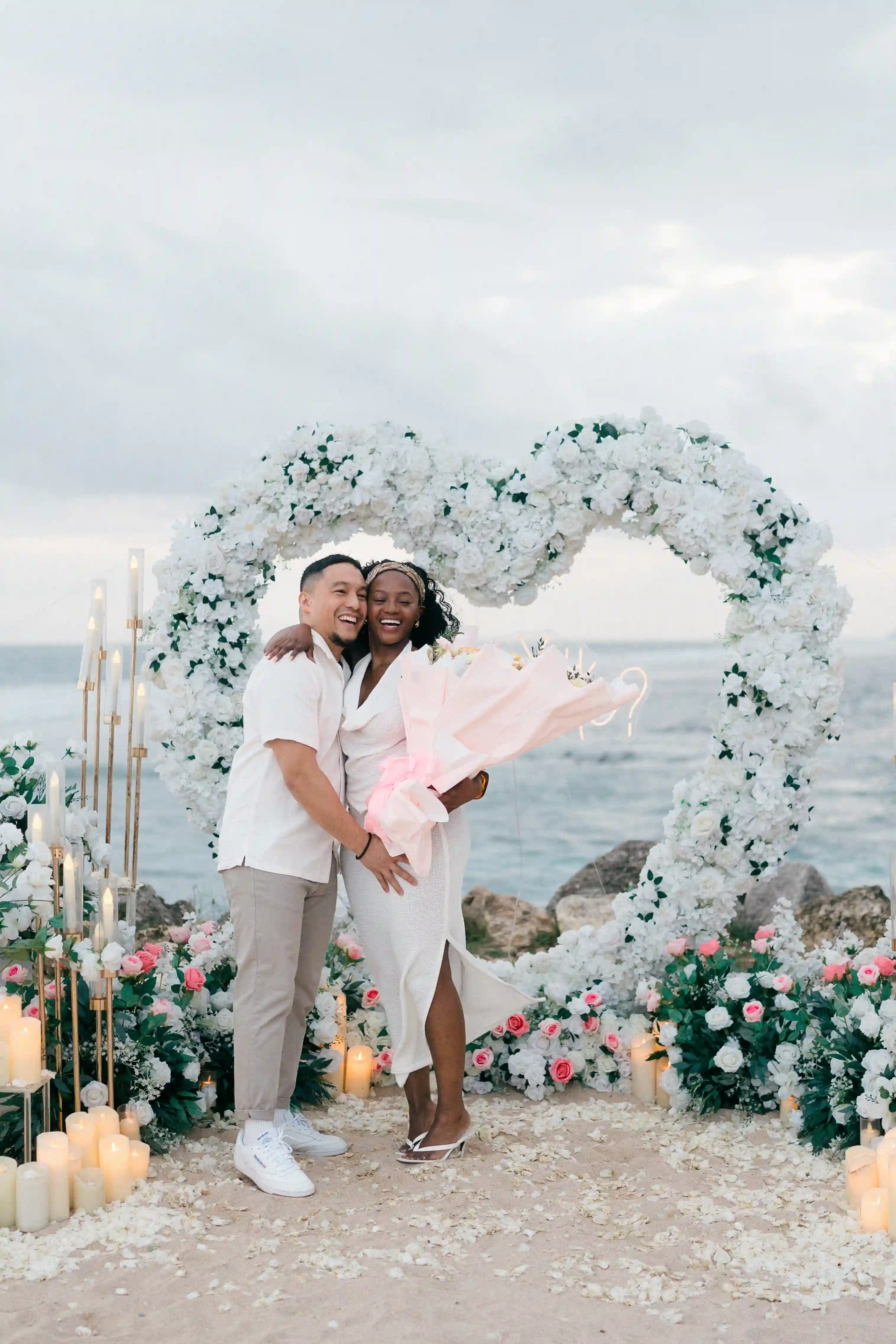 Couple kissing beneath floral heart arch overlooking the ocean