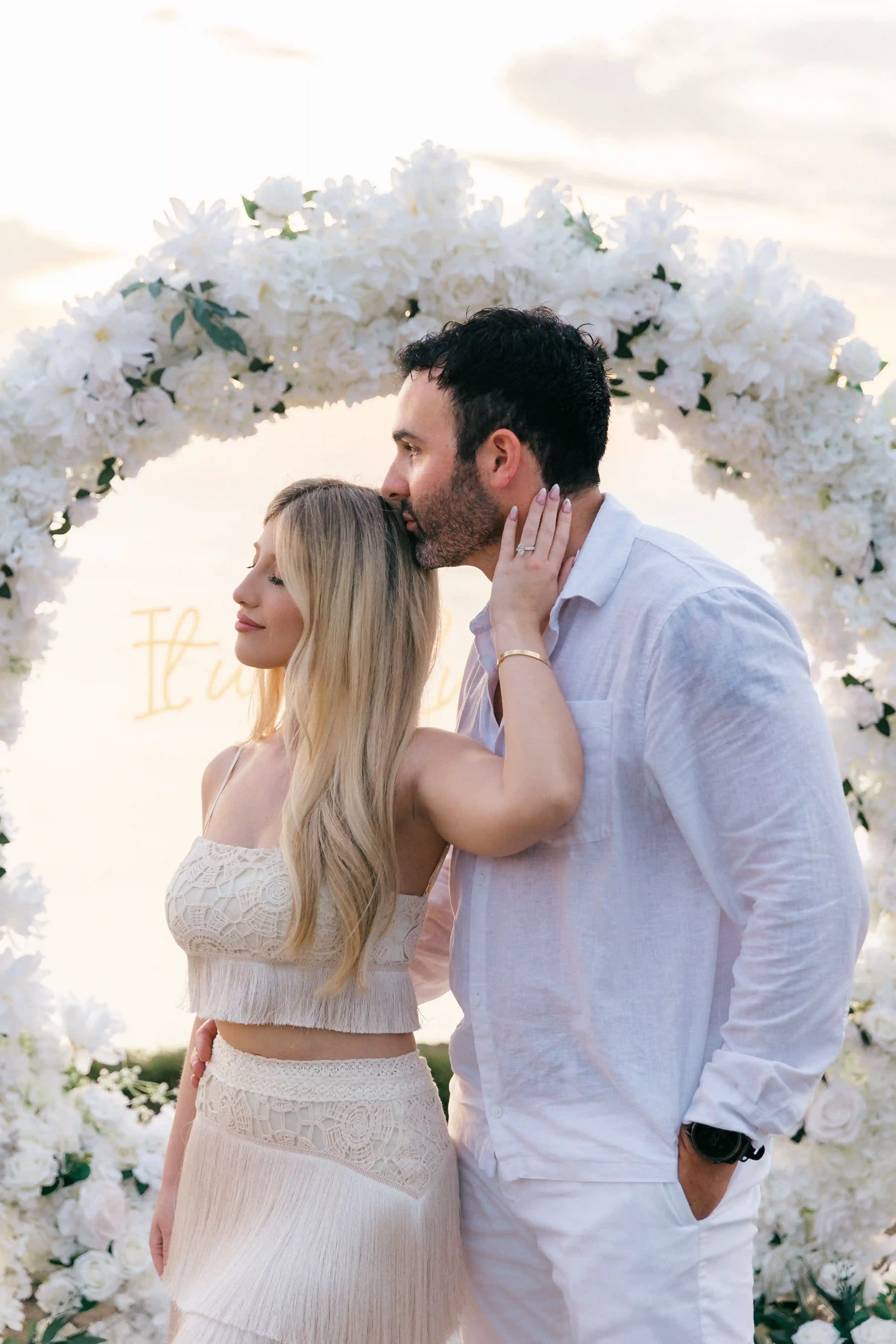 Engaged couple embracing beneath floral arch in Bali