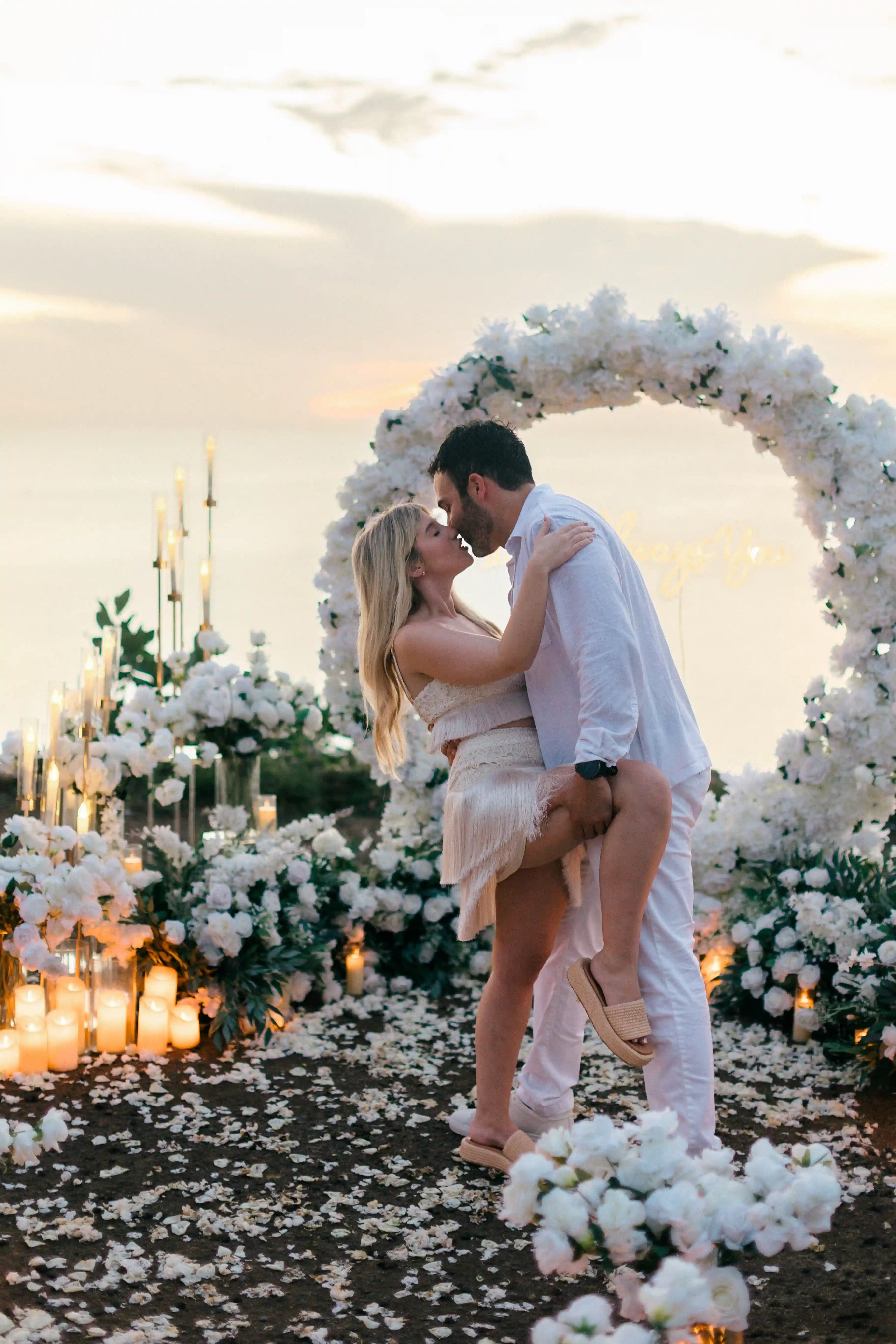 Couple kissing beneath floral arch during blue hour proposal in Bali