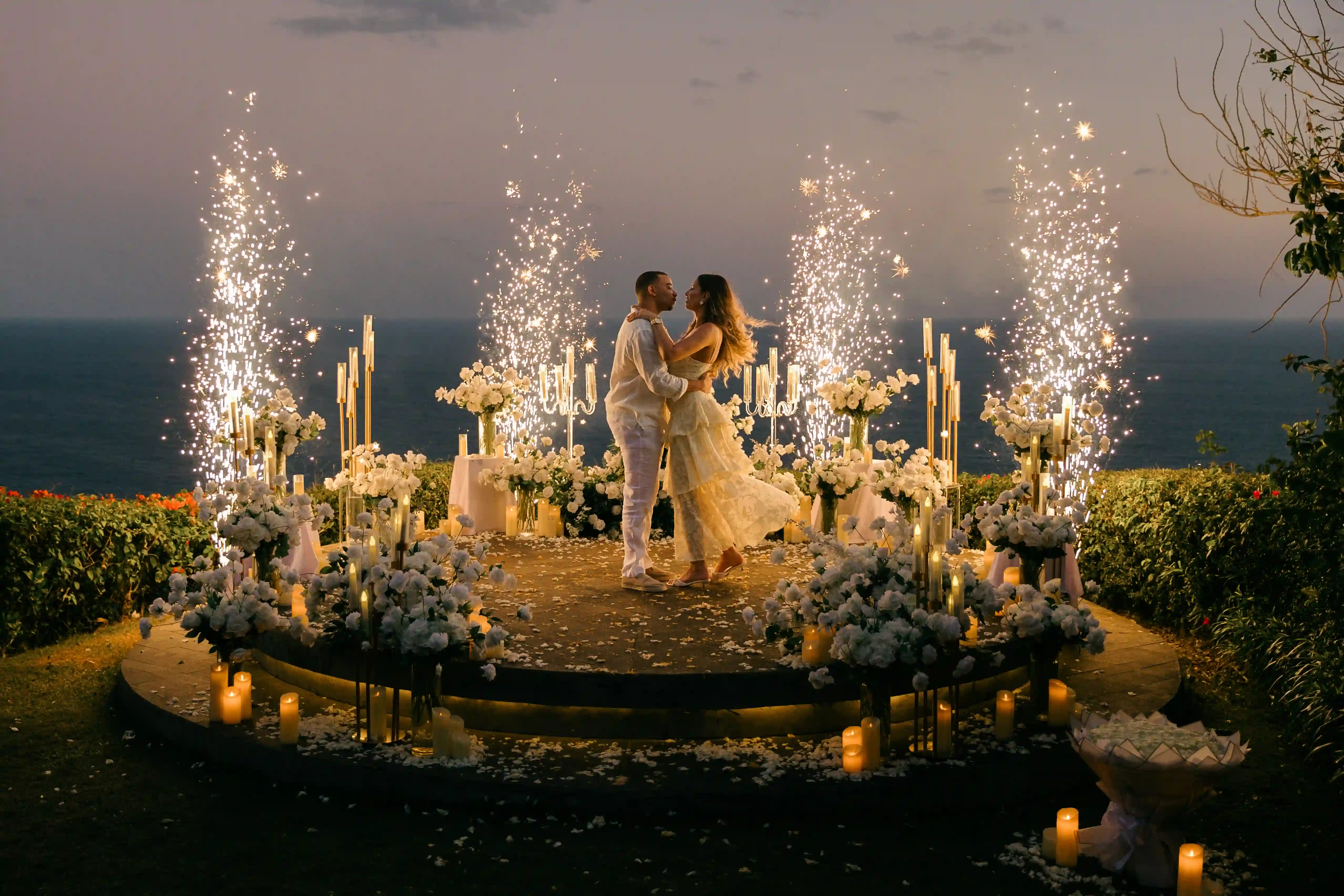Couple surrounded by sparklers at a Bali cliff proposal at dusk